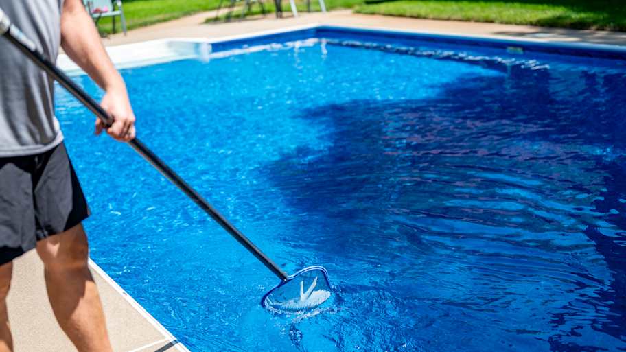 man using skimmer to clean pool