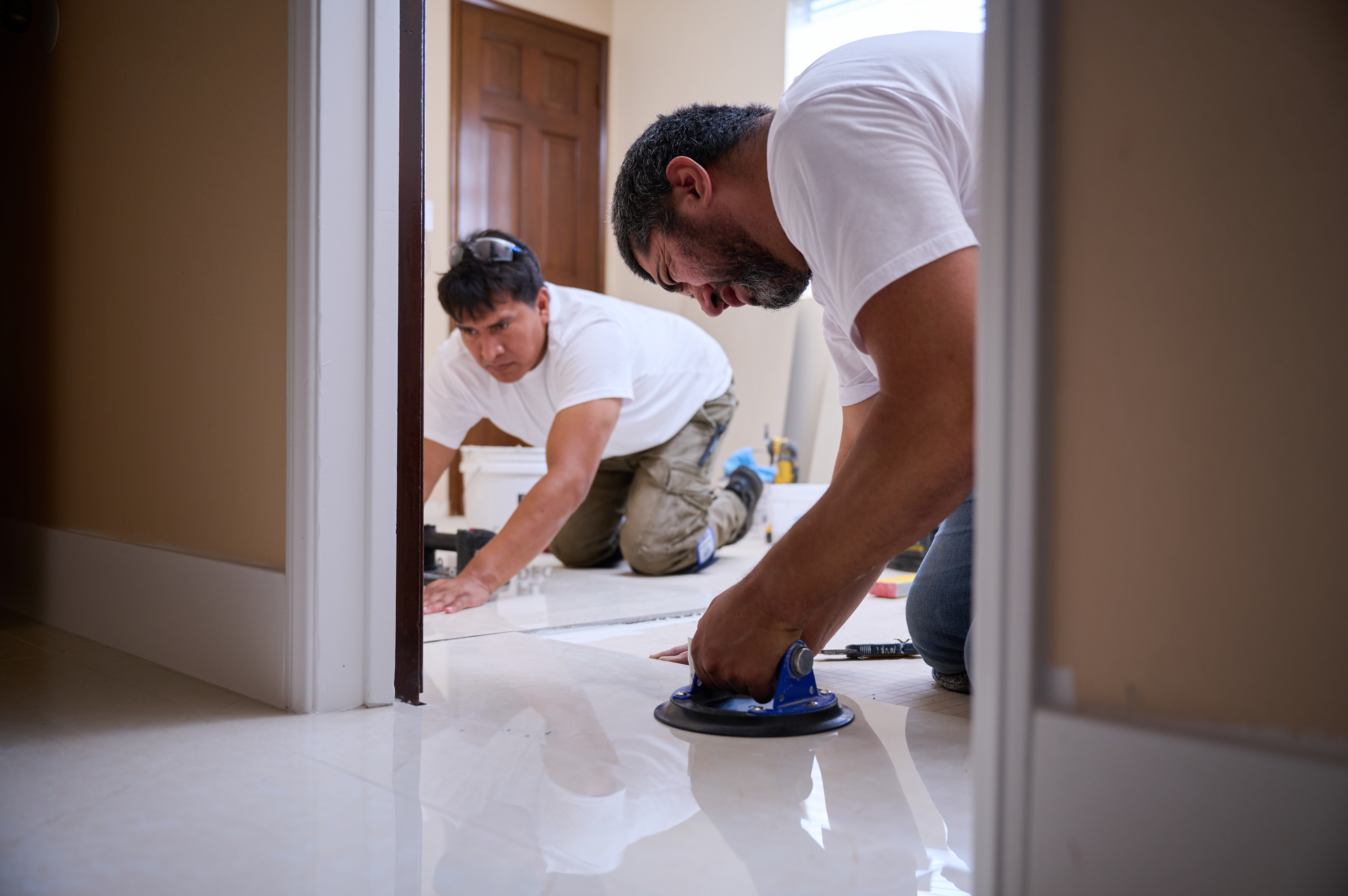 Two workers carefully position and adjust floor tiles with a suction tool, ensuring accurate alignment and a seamless finish.