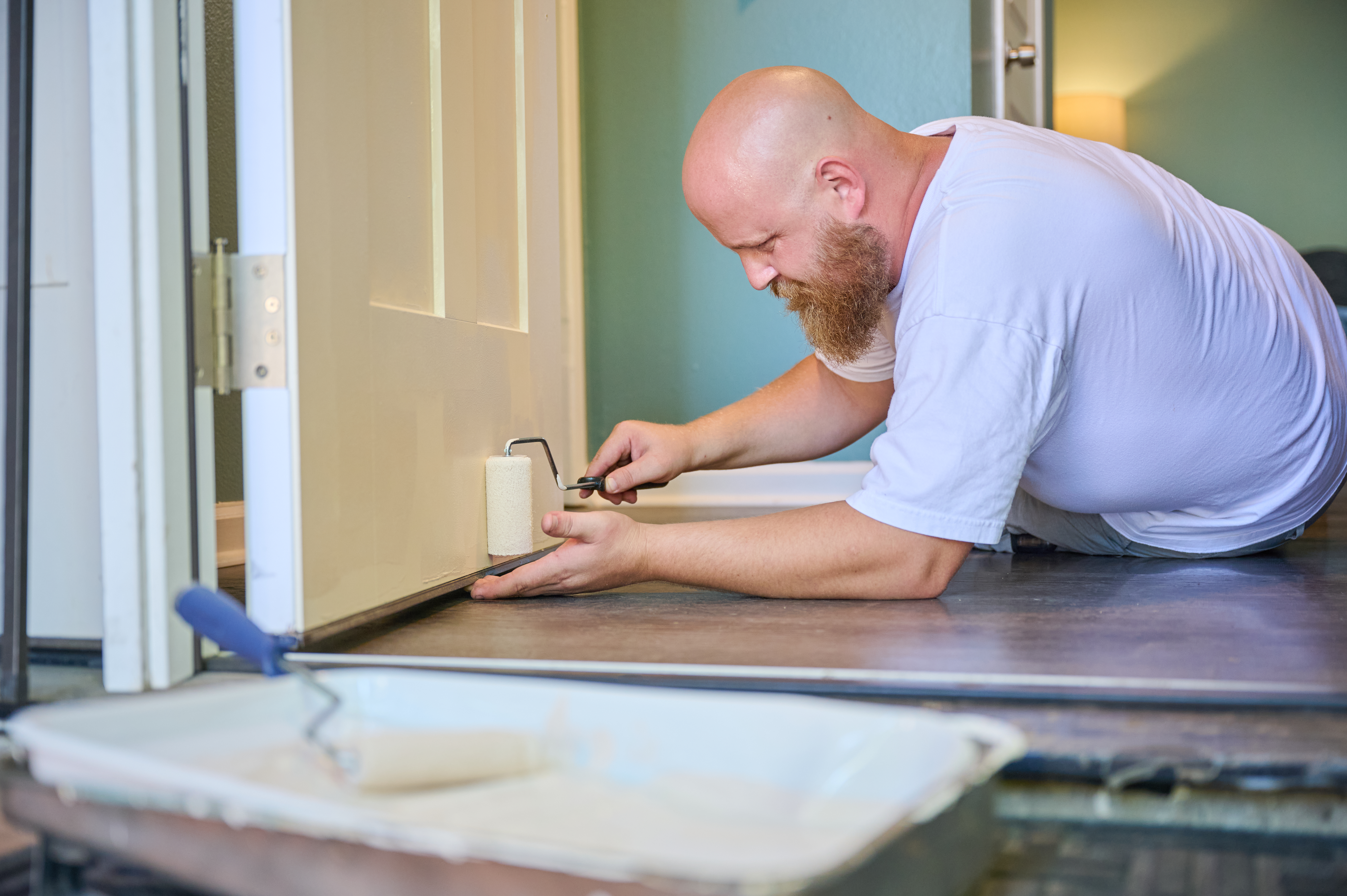 Handyman Chris McNeill from C.A. Shamrock LLC  uses a small roller to carefully paint the bottom edge of a door while lying on the floor for precision.