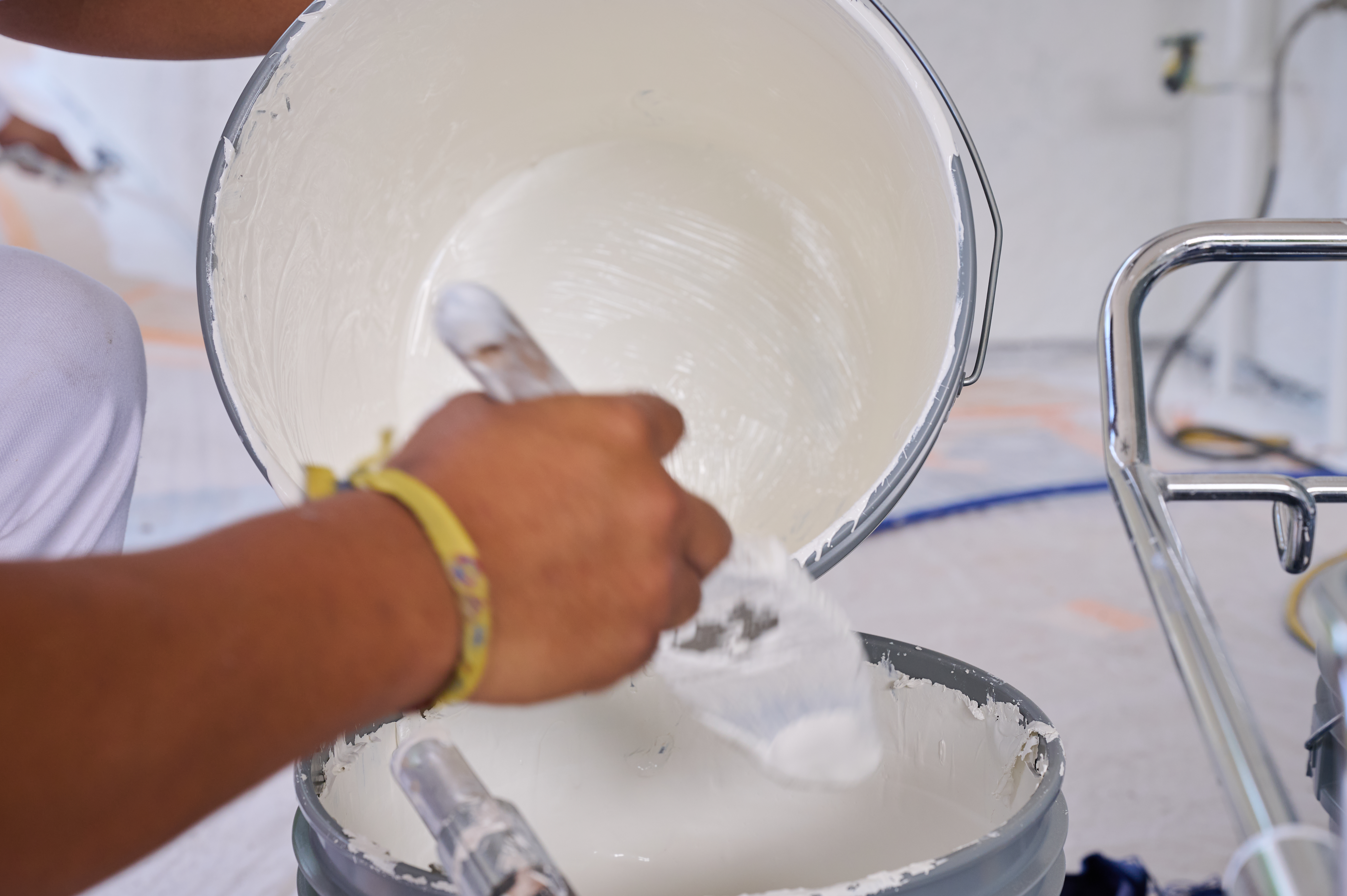 Close-up of painter’s hand pouring white paint into a bucket, preparing for an exterior painting project.