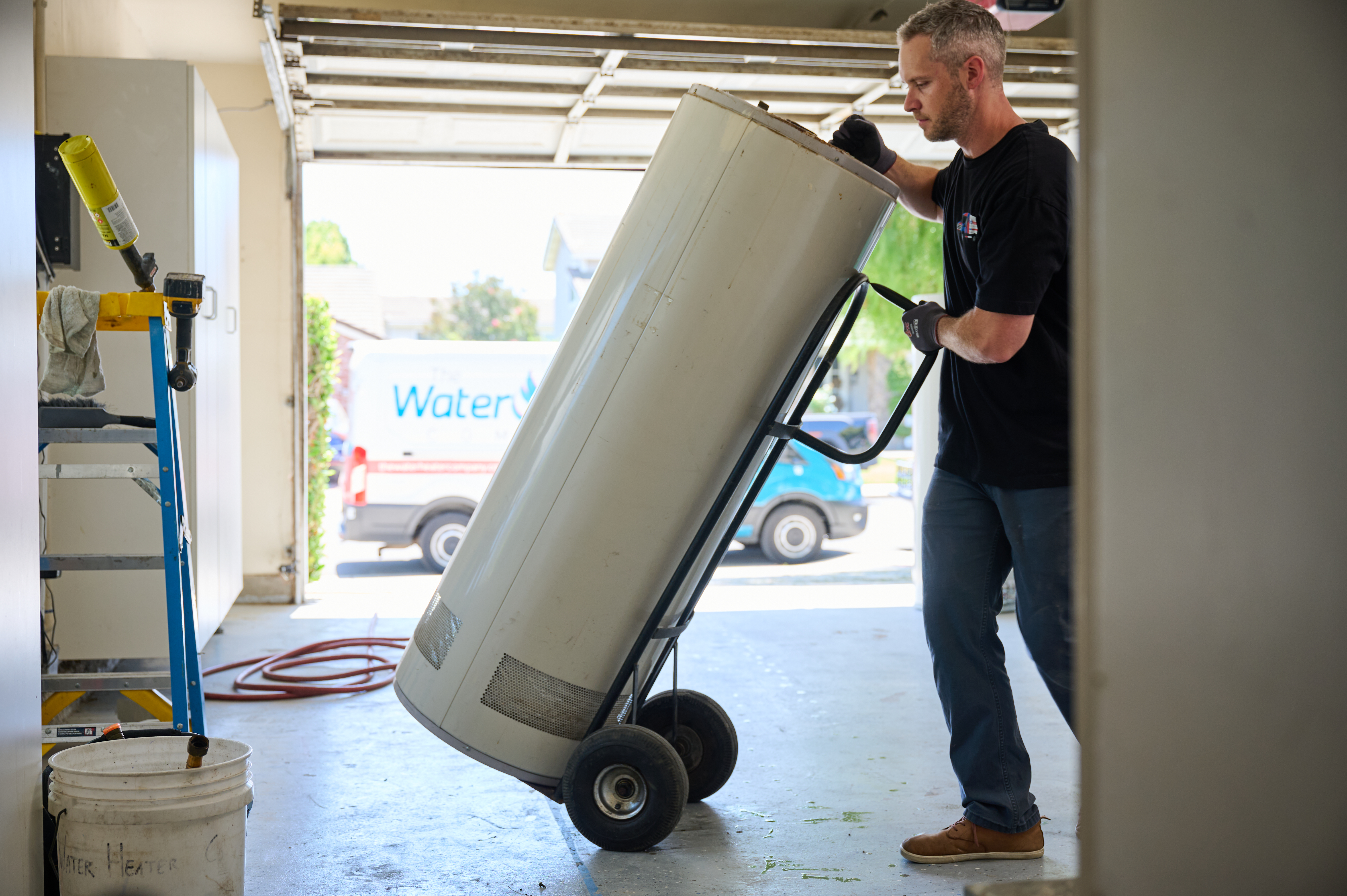 Technician carefully maneuvers a water heater on a dolly in a garage, preparing for installation or removal.