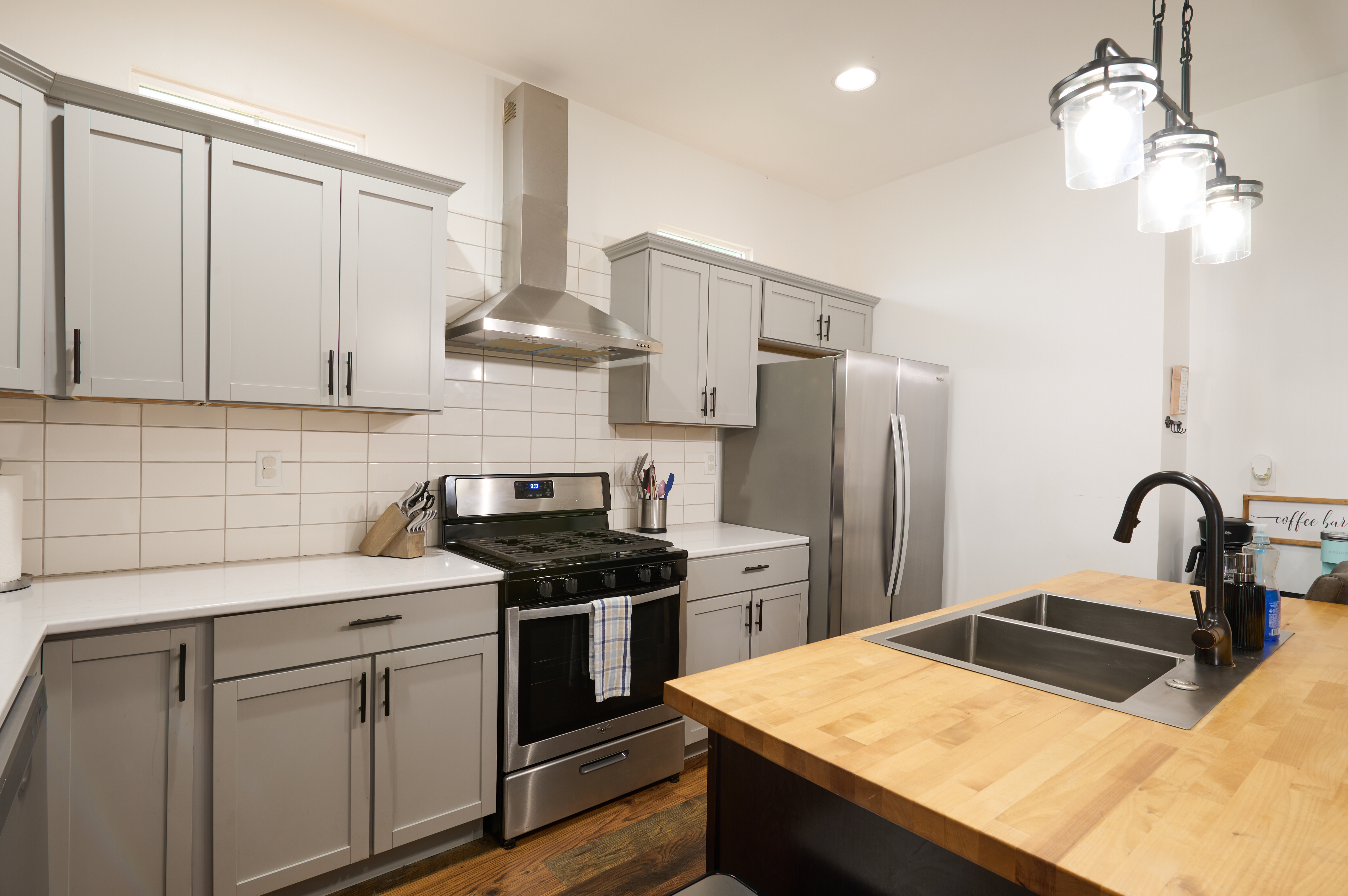 Modern kitchen with gray cabinets, a stainless steel oven and refrigerator, tile backsplash, and a wood island countertop.