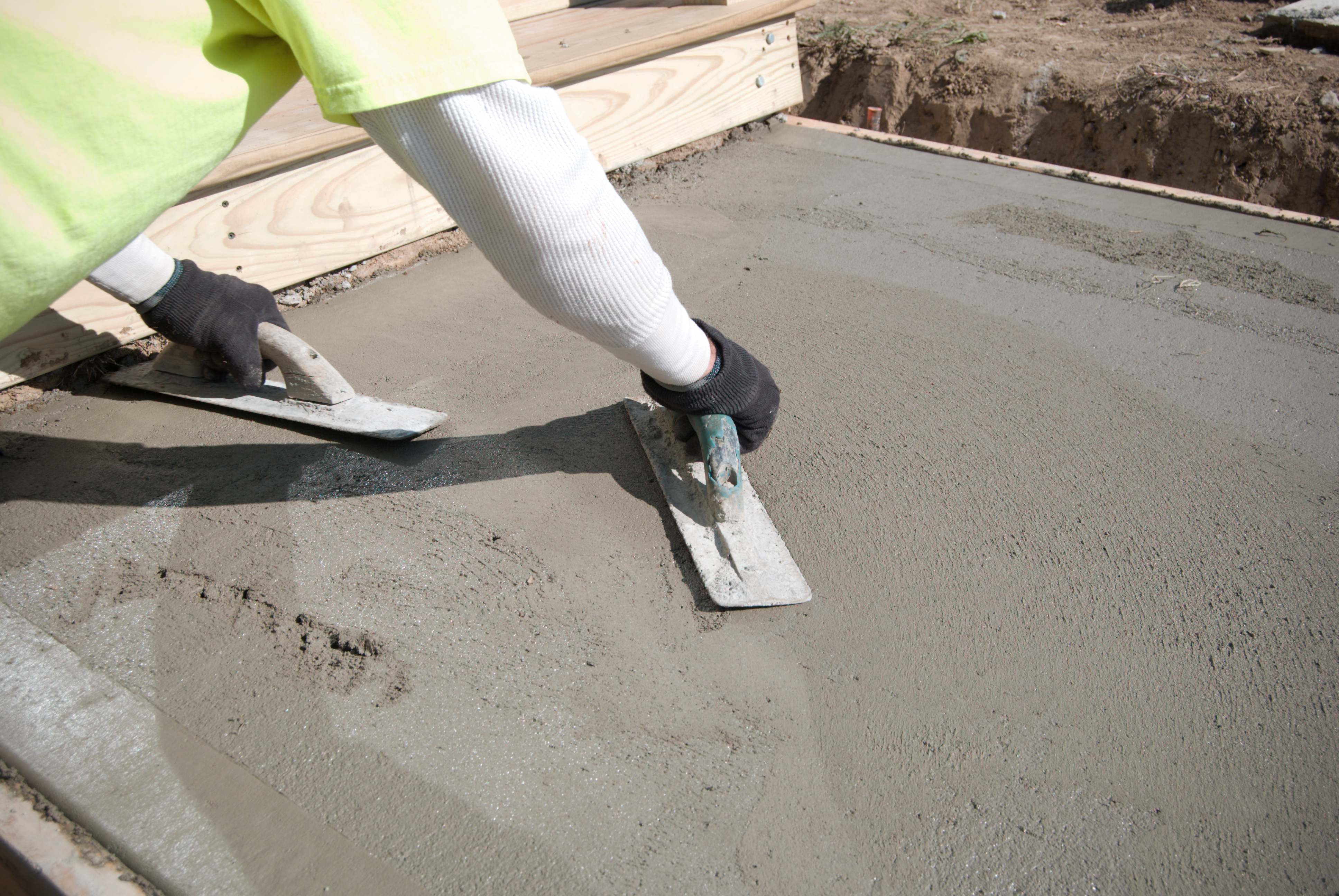 A worker smooths the surface of a freshly poured concrete sidewalk, ensuring a durable and clean walking path at a house.