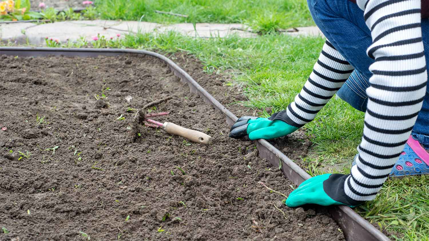 A woman installs edging in a garden