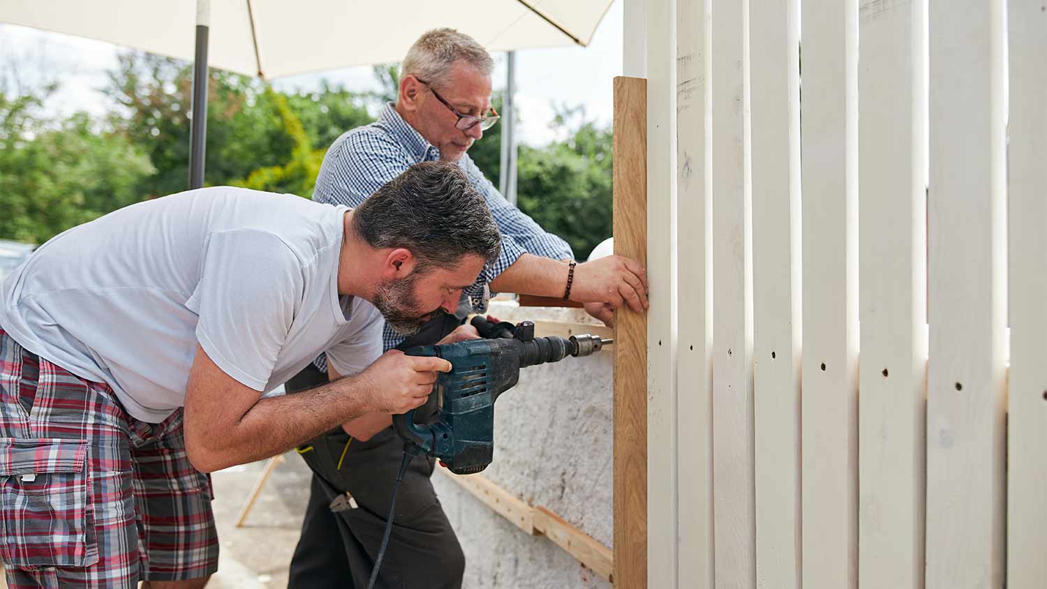 two men installing wood fence in yard