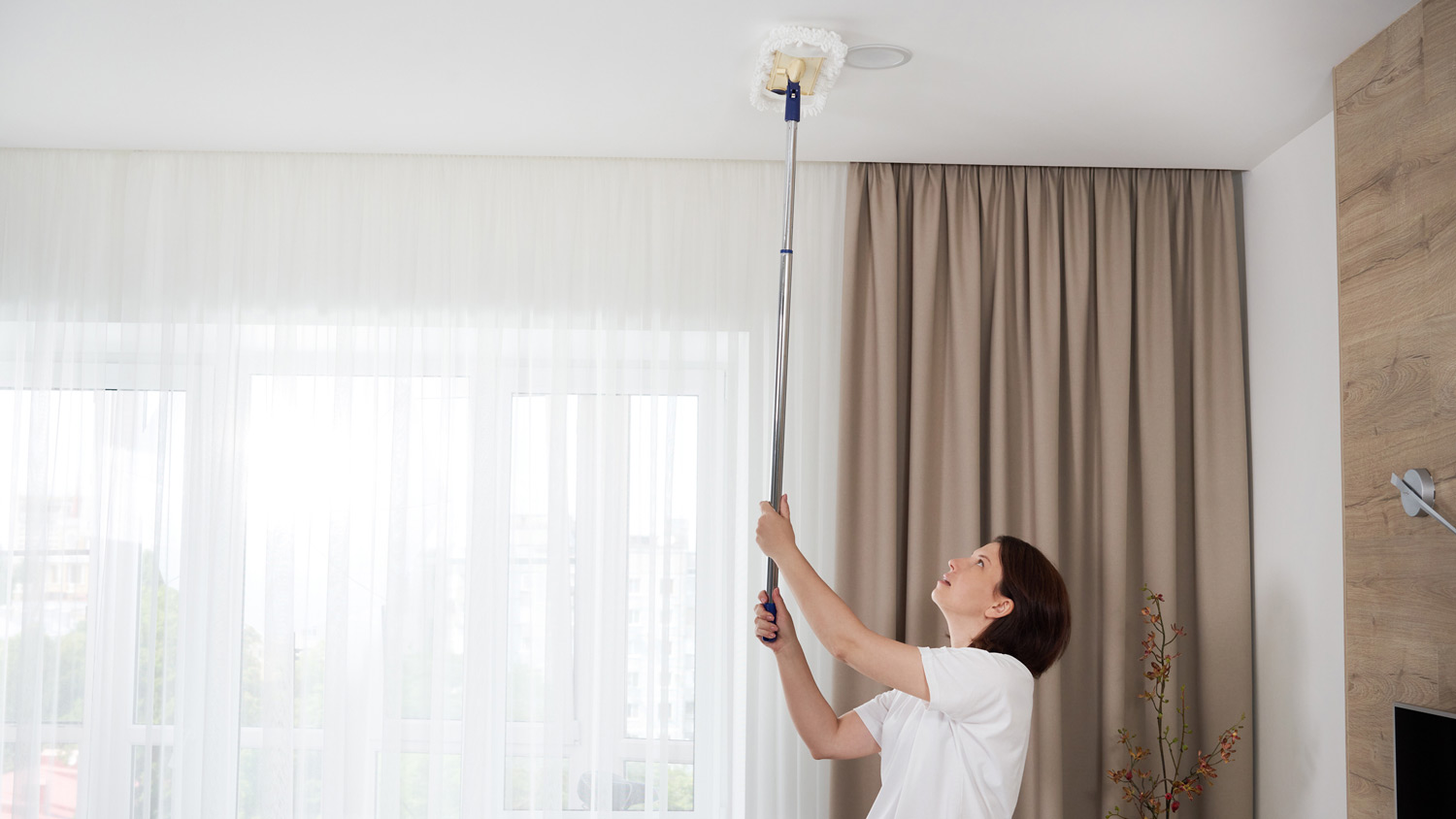 A woman with a mop cleaning a room’s ceiling