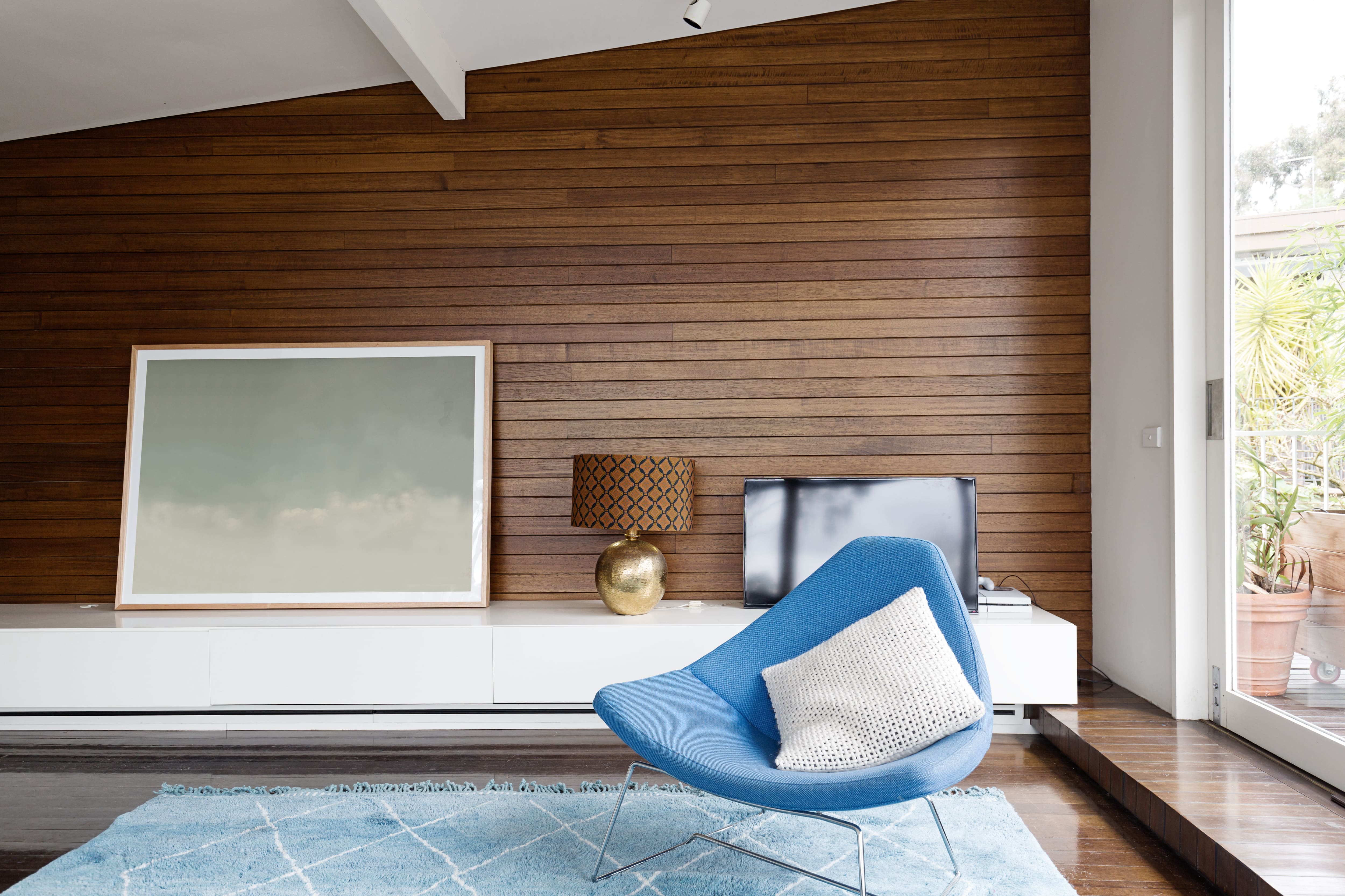 Slanted tongue and groove wood wall paneling in mid century modern living room with blue modern chair