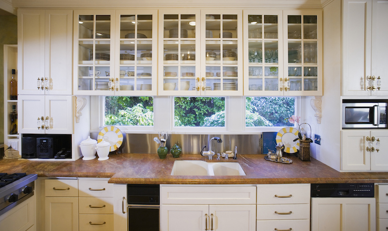 kitchen with windows, wood countertop, and cream cabinets with glass