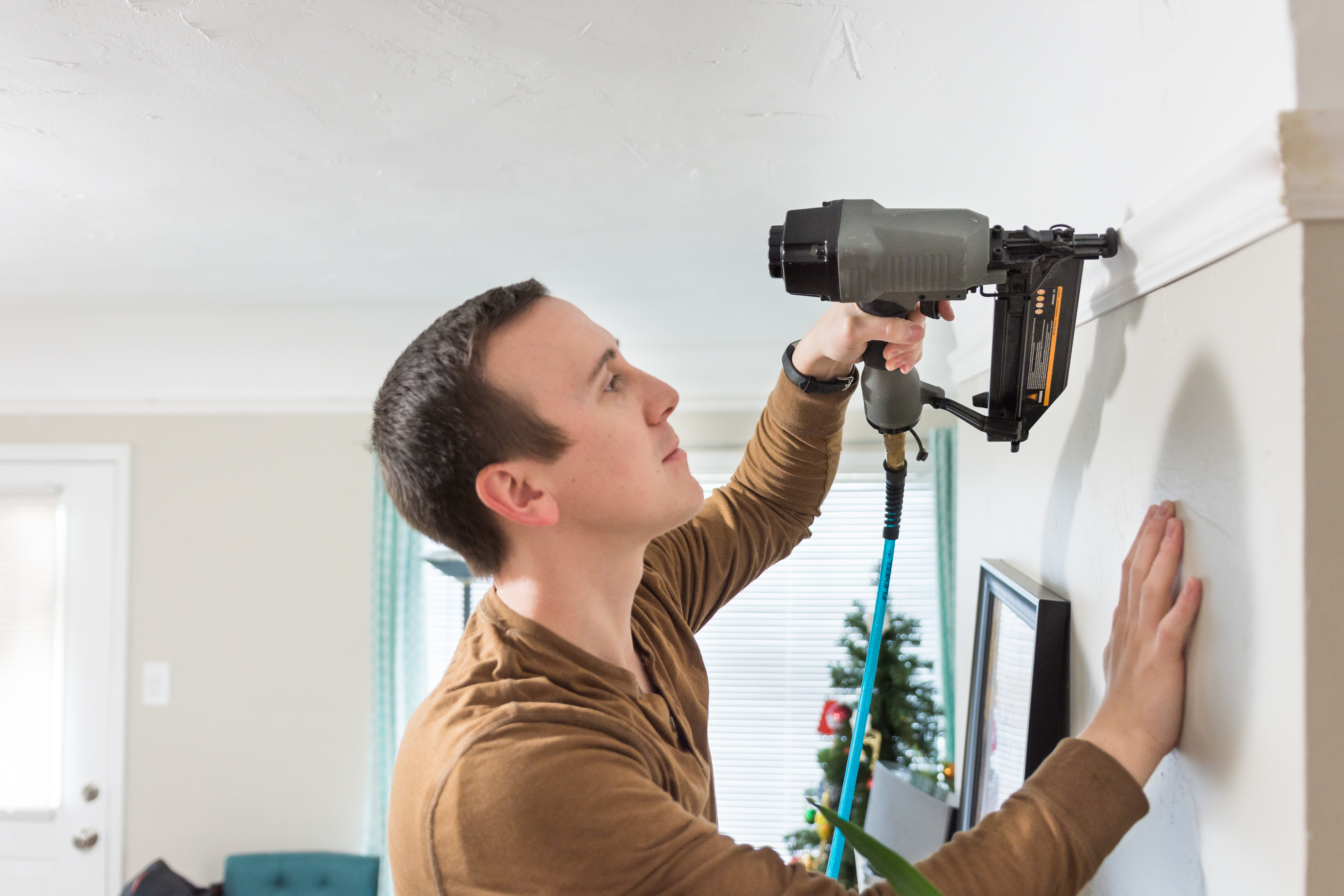 A man installing a crown molding using a nail gun 