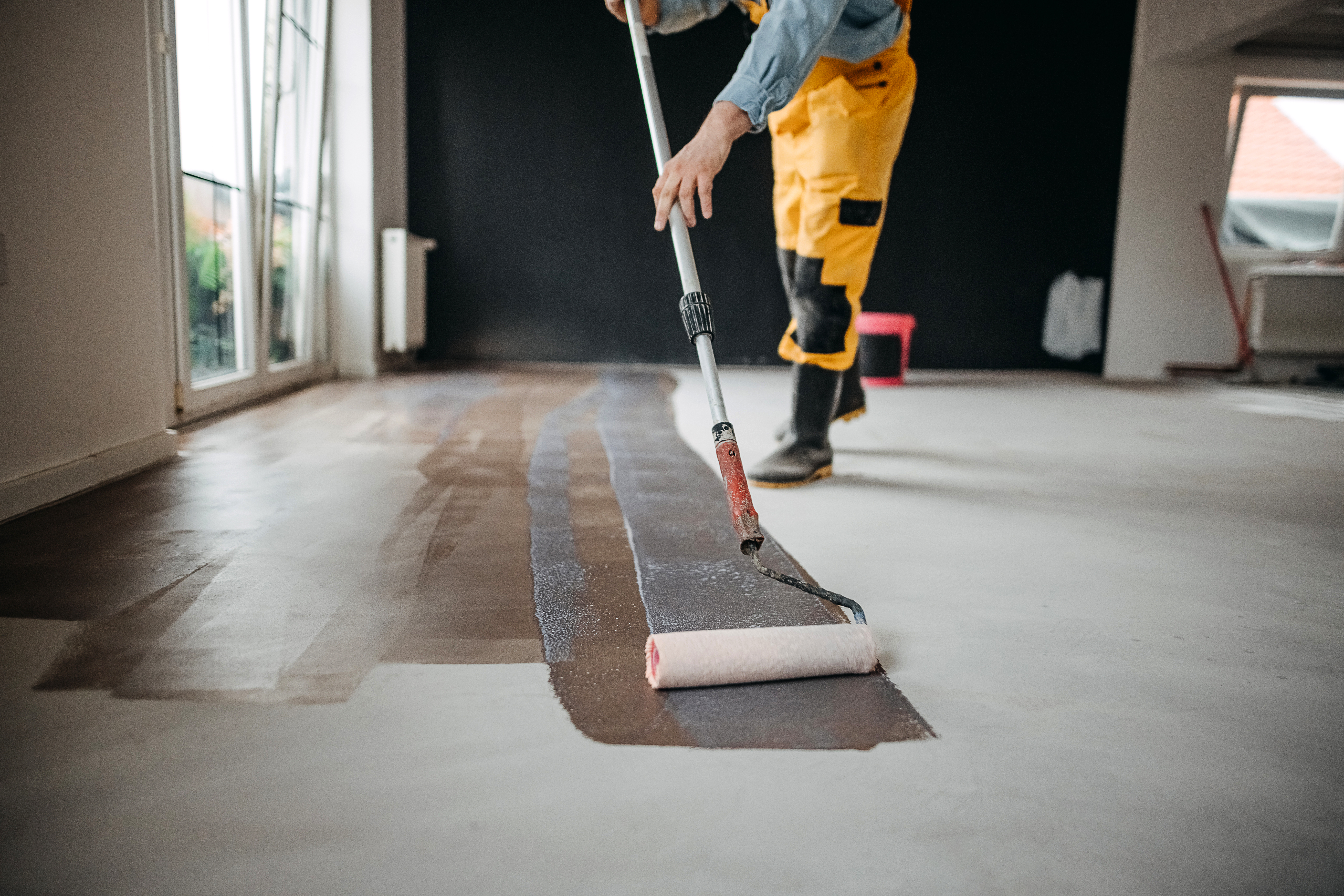 Worker paints under the apartment with a roller.