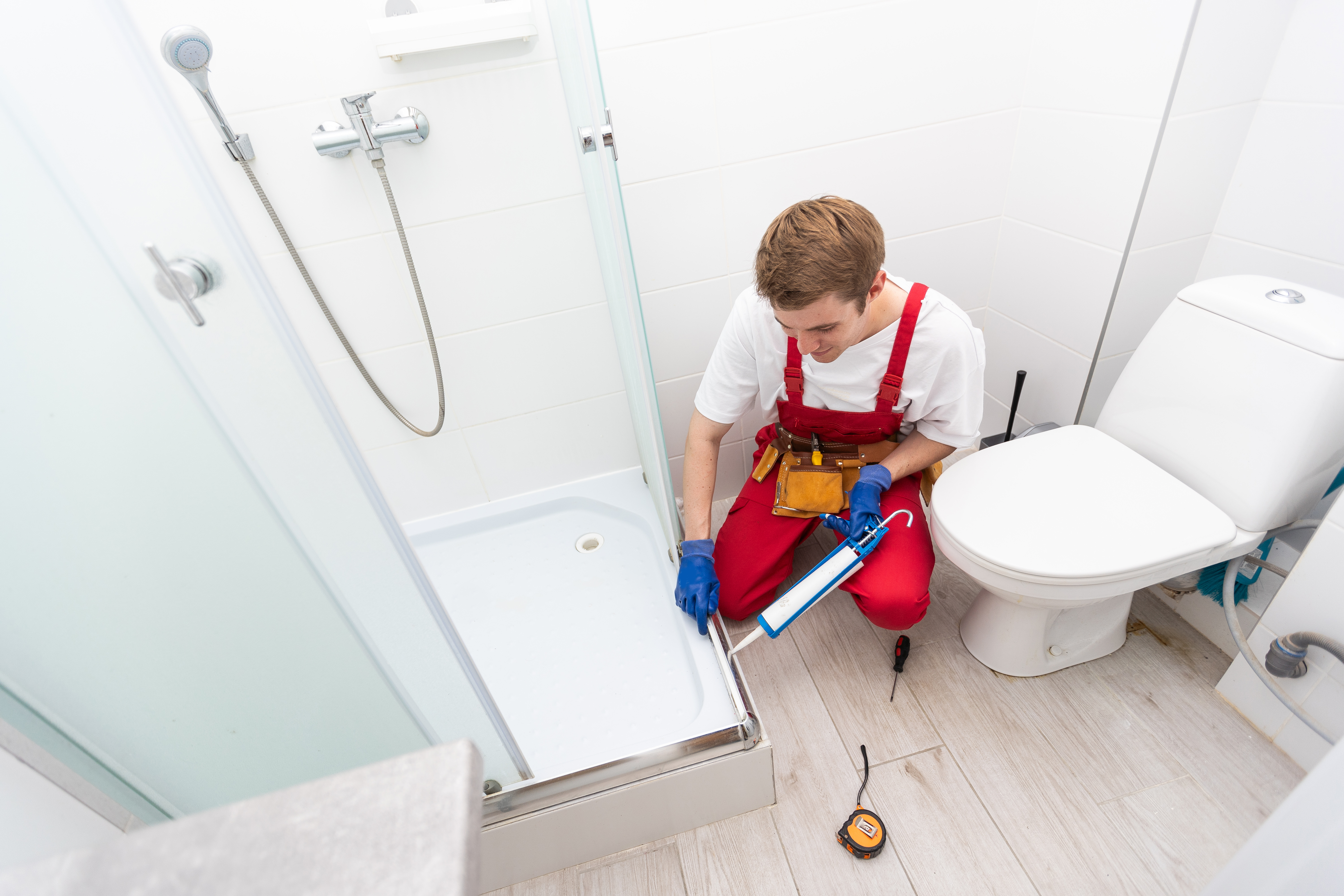 Handyperson using waterproof silicone to seal a shower door 