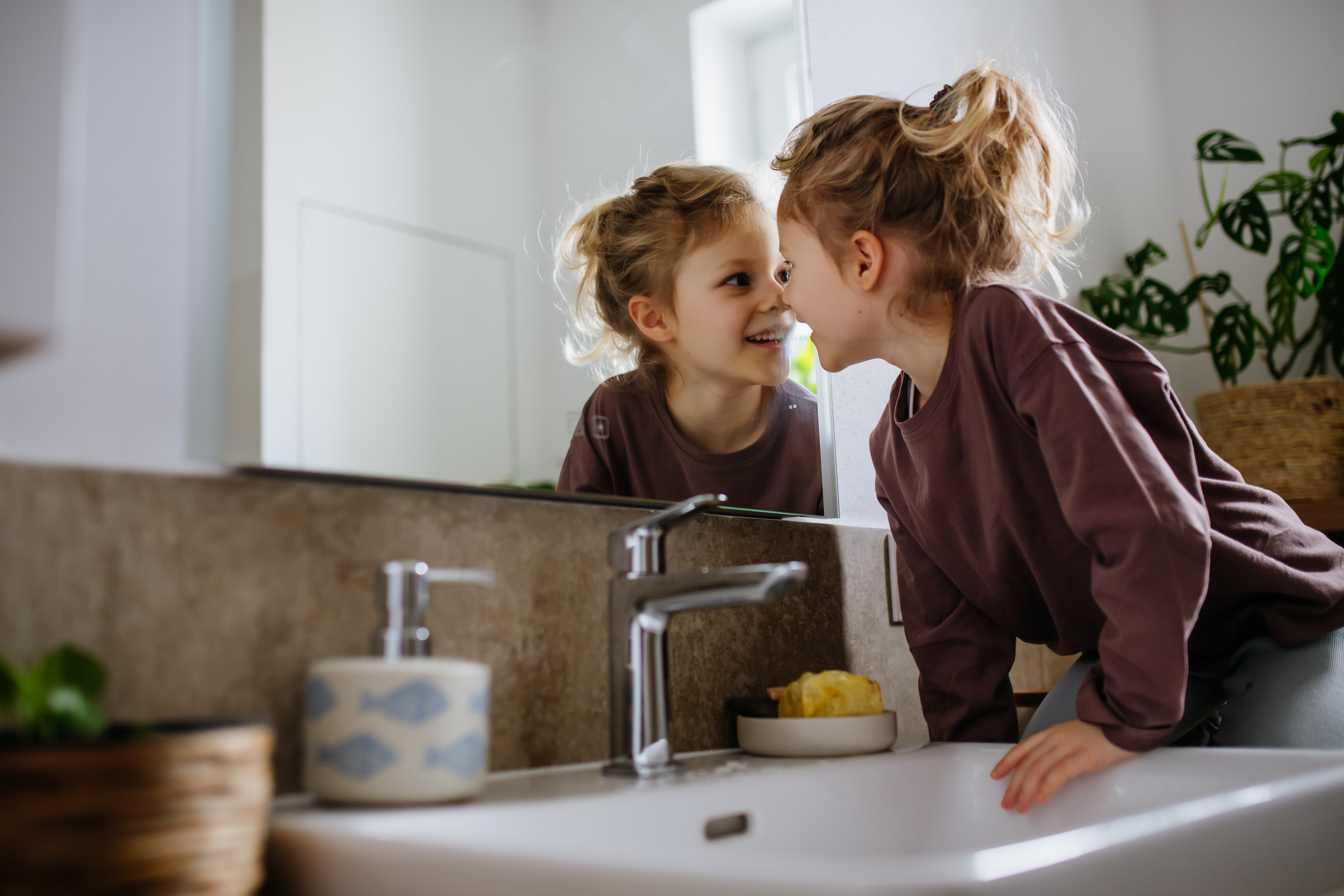 Little girl sitting in the bathroom, looking at her reflection