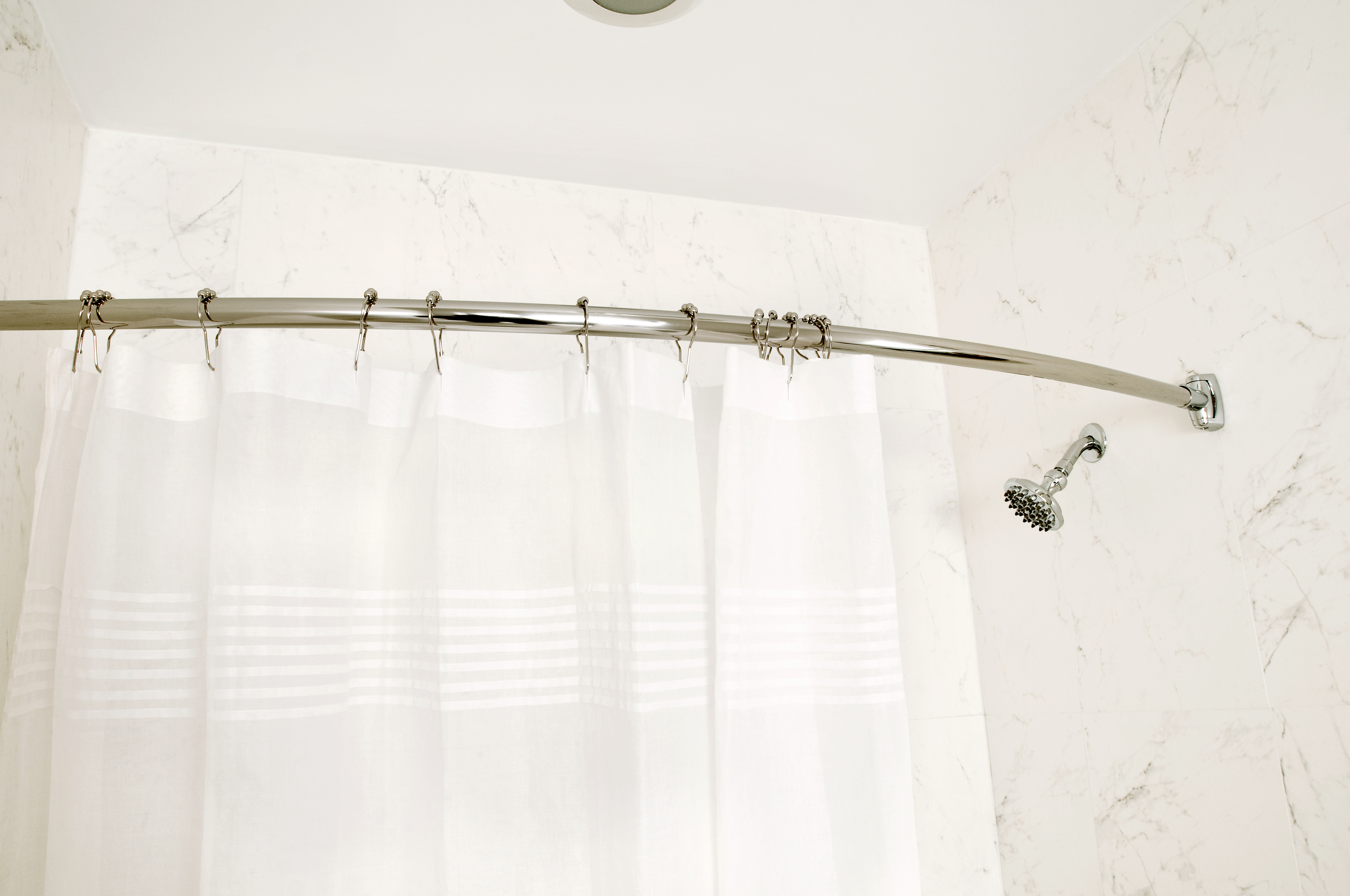 White shower curtain hanging from a chrome rod 