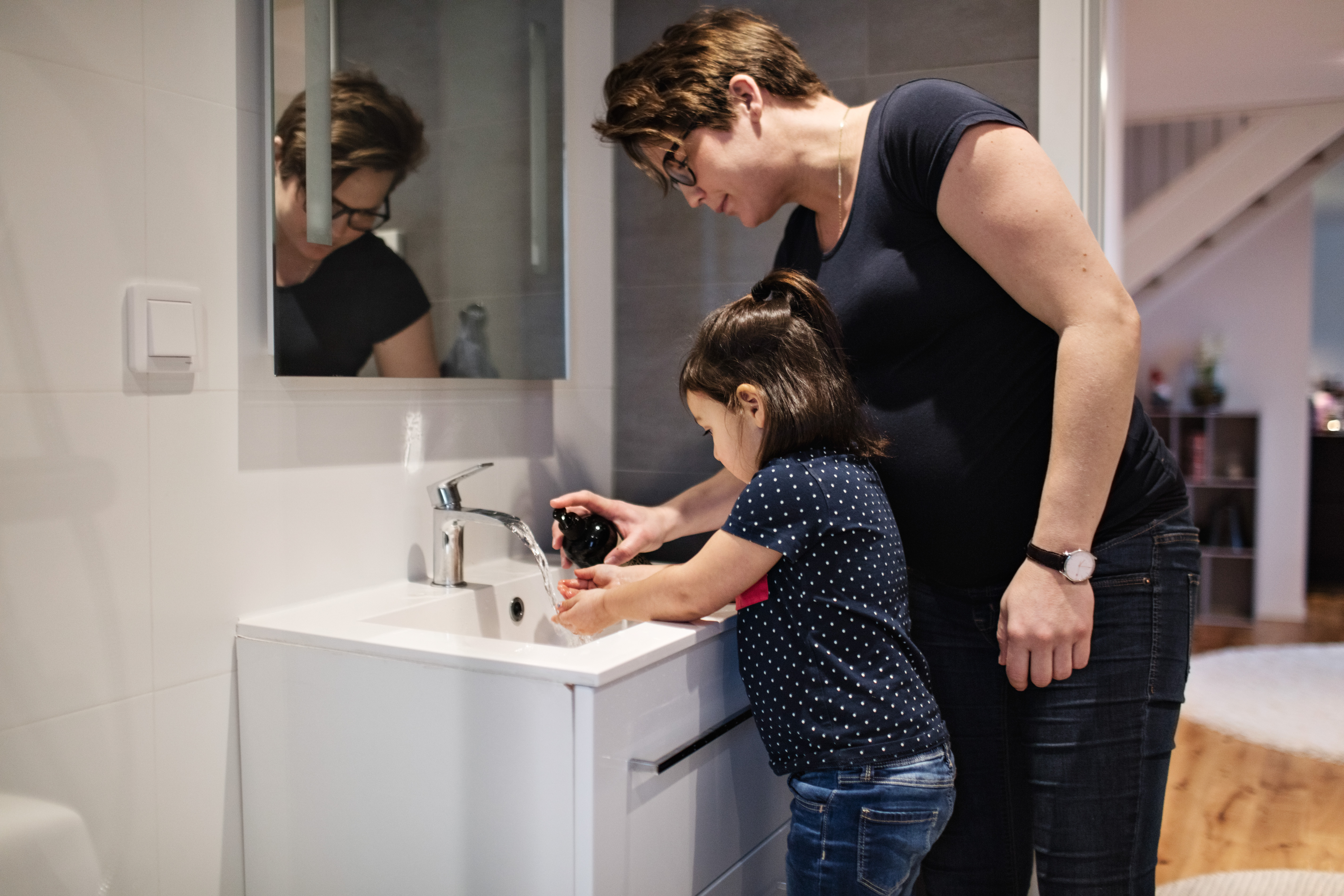 Mother helping daughter wash her hands in the bathroom 