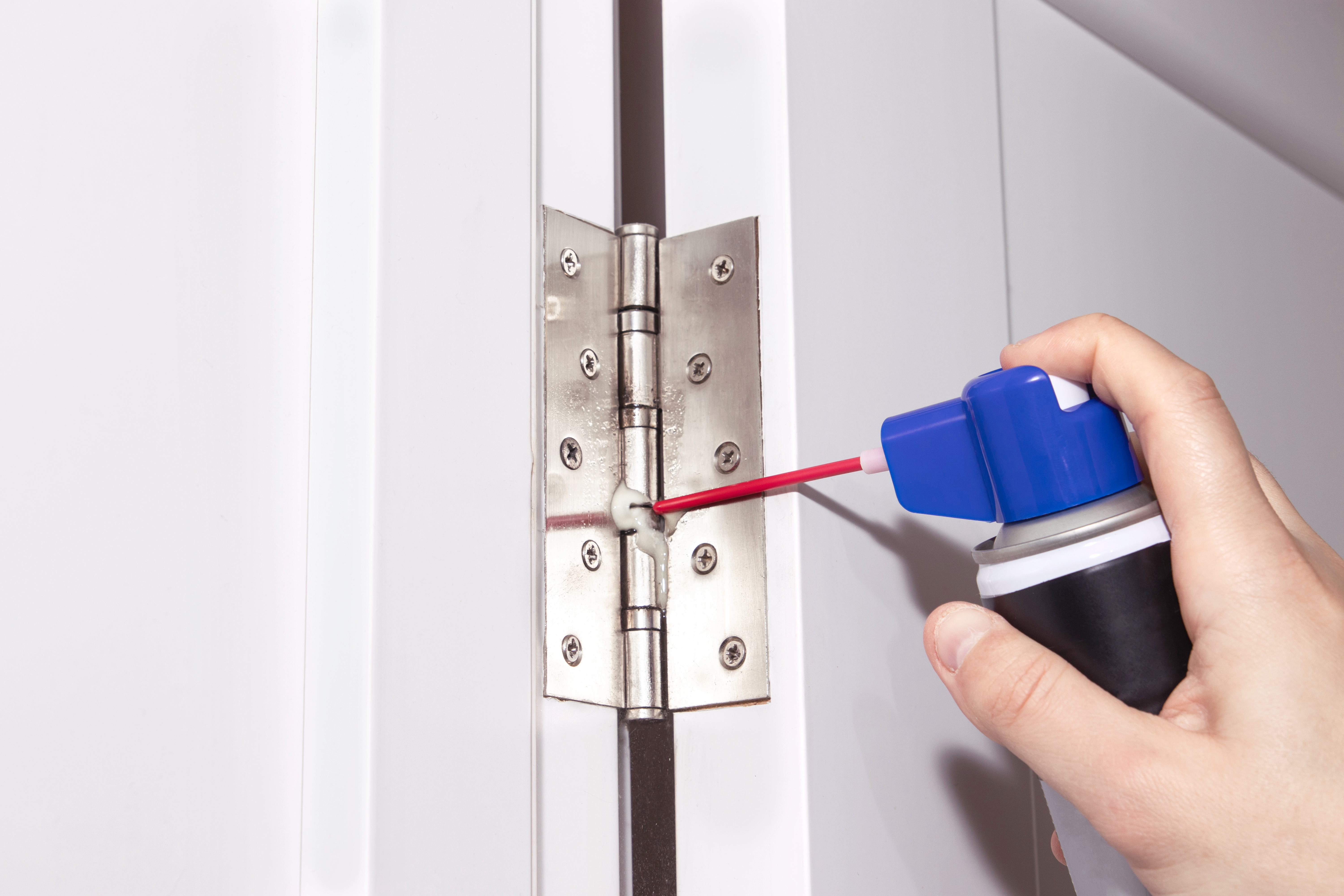 Person using spray to grease a door hinge