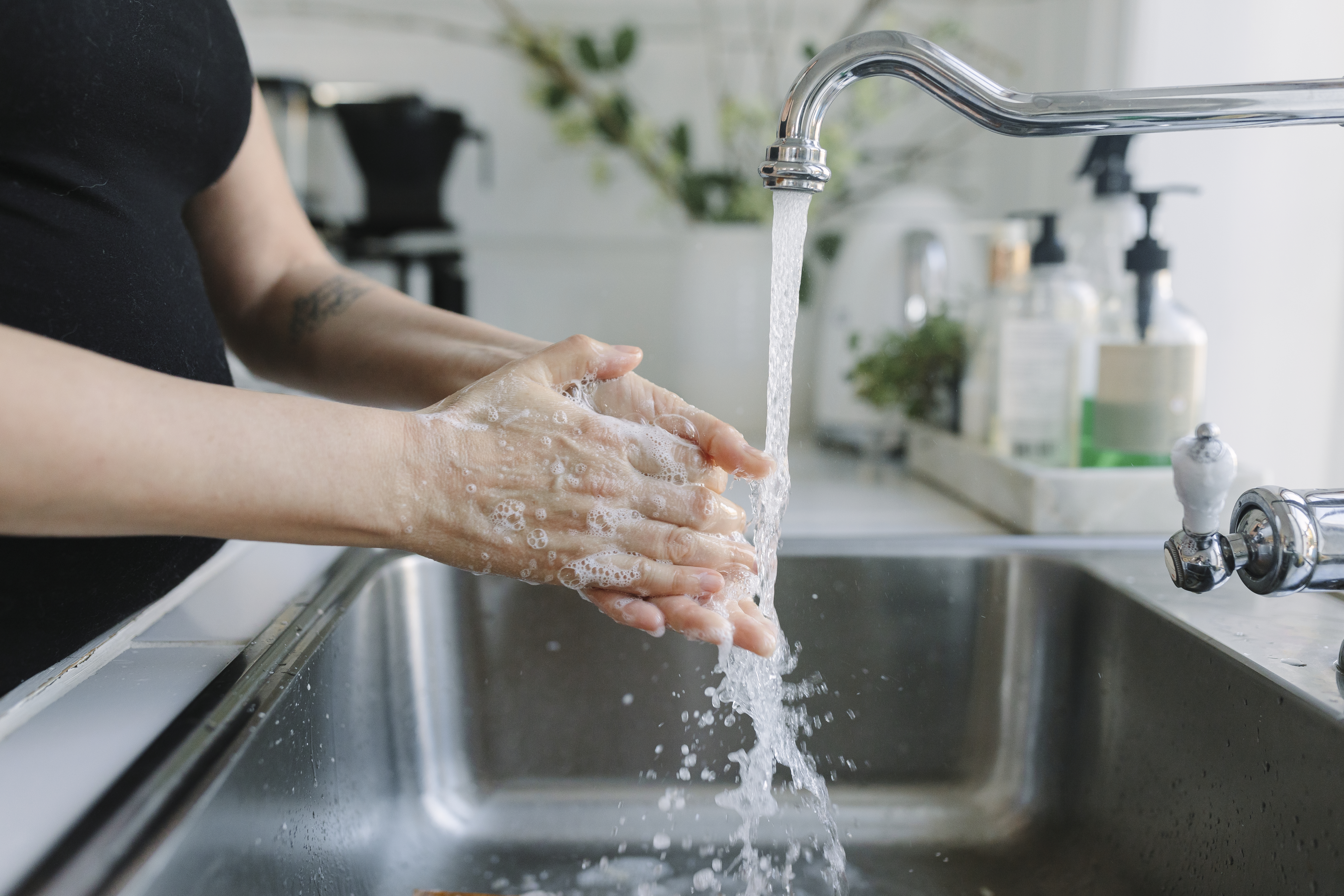 Woman washing her hands in a stainless-steel kitchen sink  