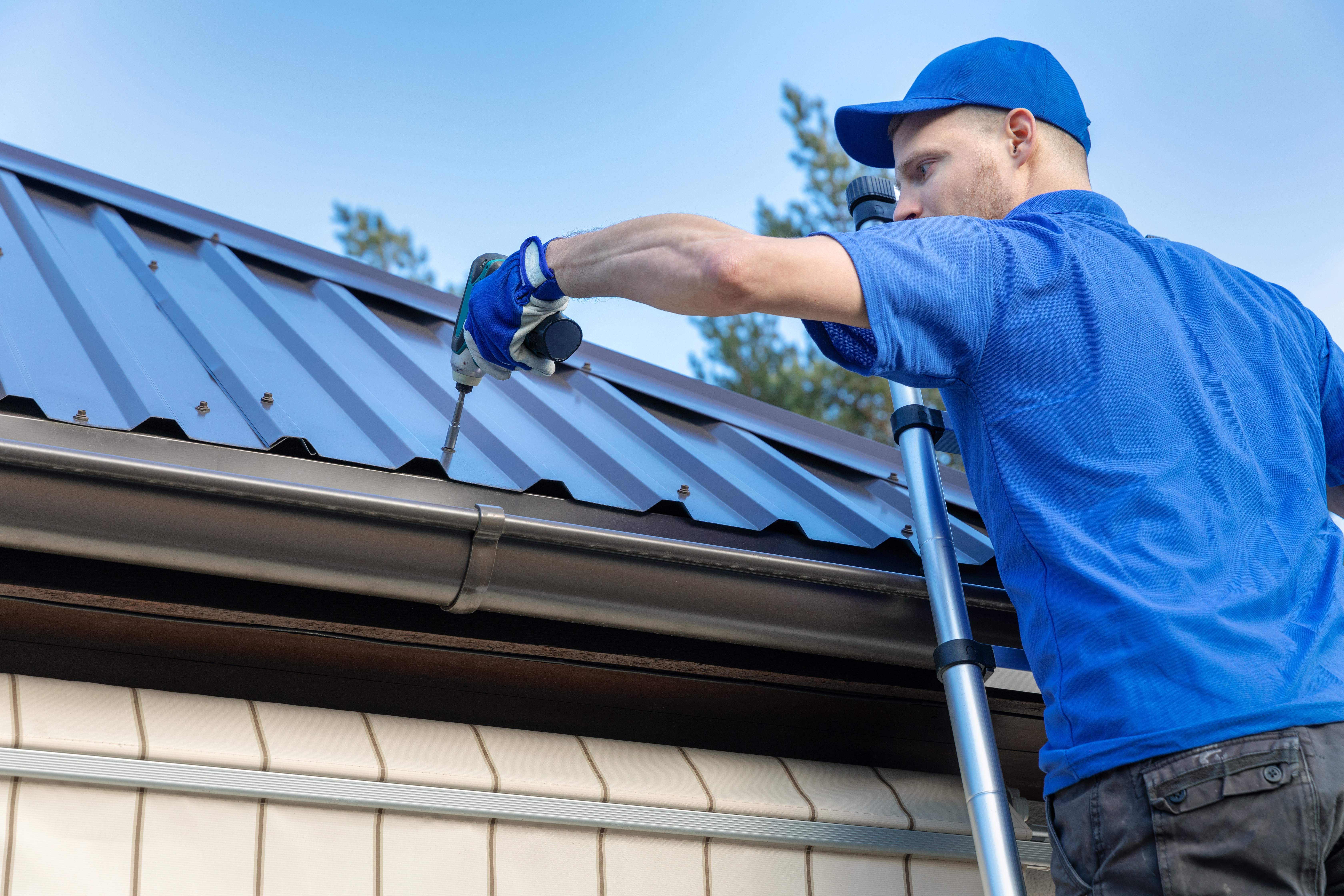 Roofer on a ladder installing a new metal roof on a house