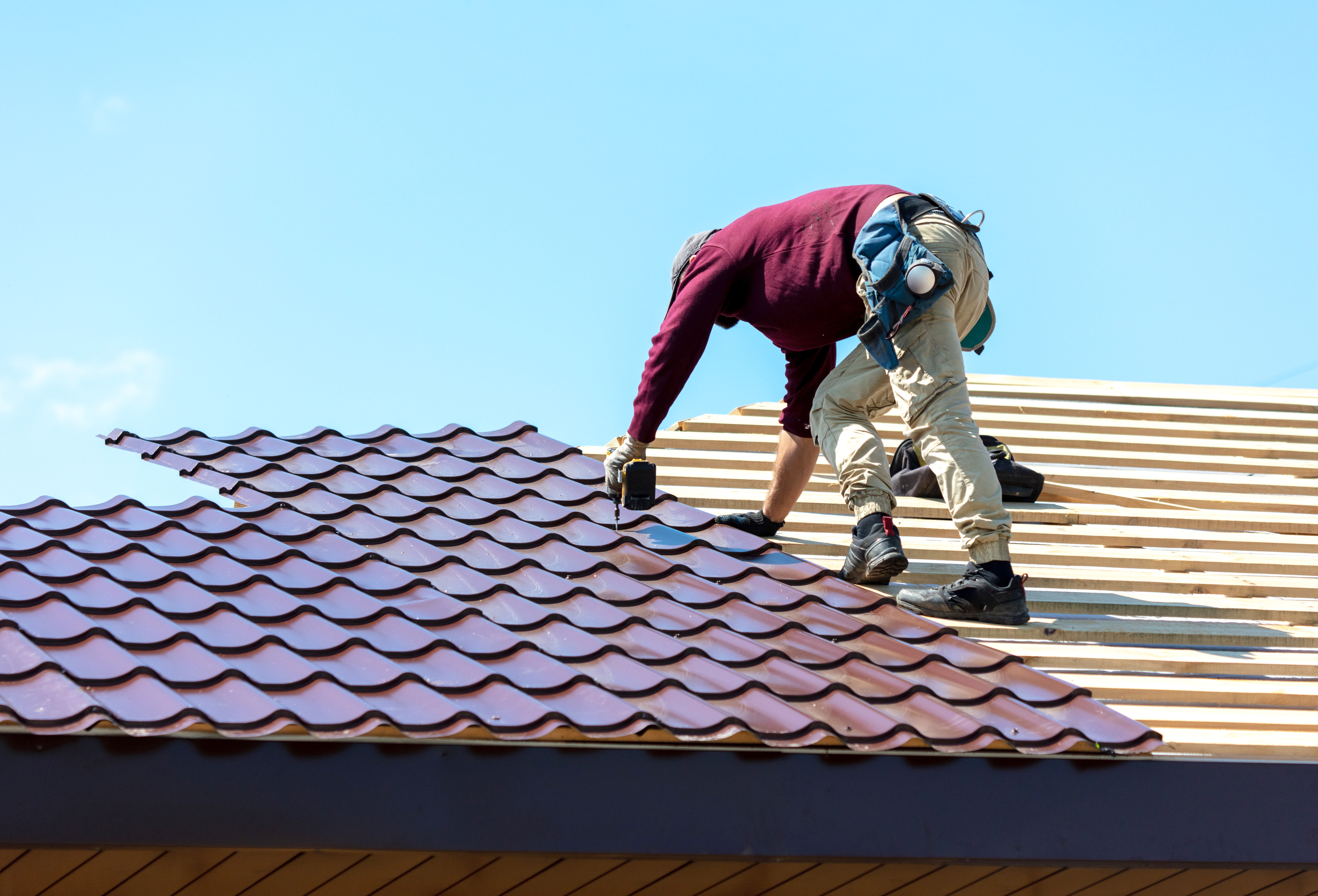 Contractor installing red metal tiles on the roof of a house