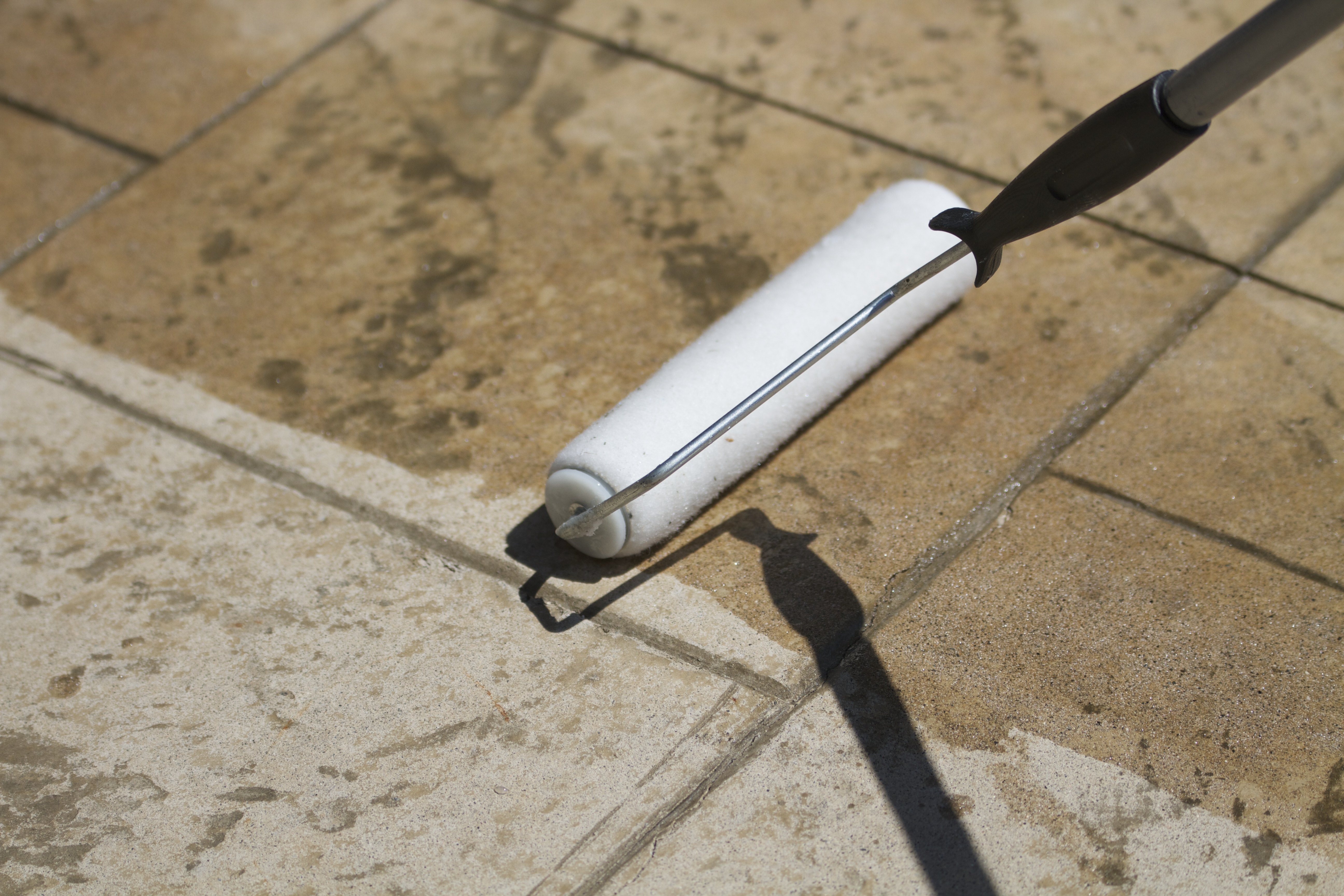 A paint roller is being used to apply a clear sealant