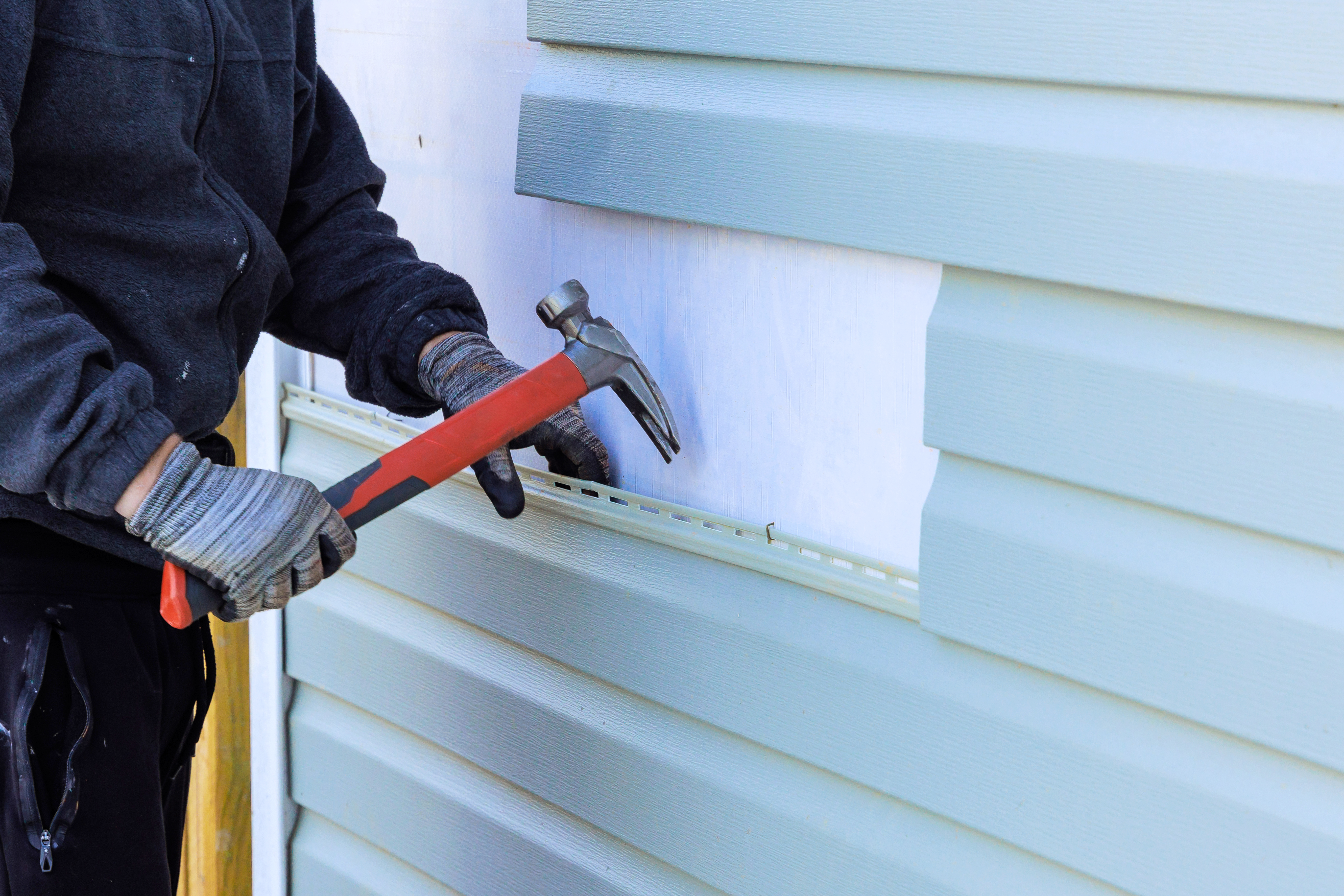 Worker removing old vinyl siding from the house