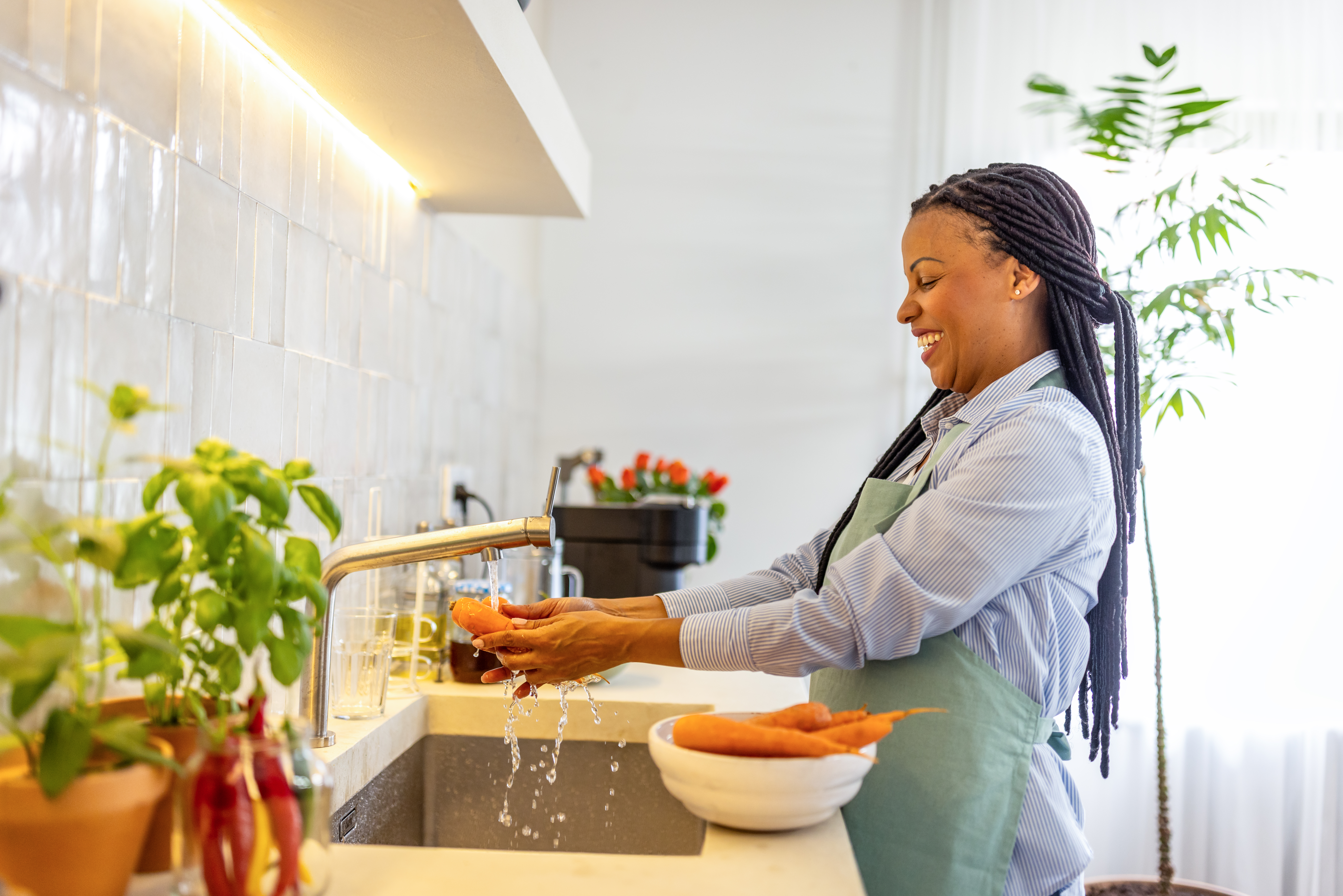 Smiling woman washing carrots in the kitchen sink