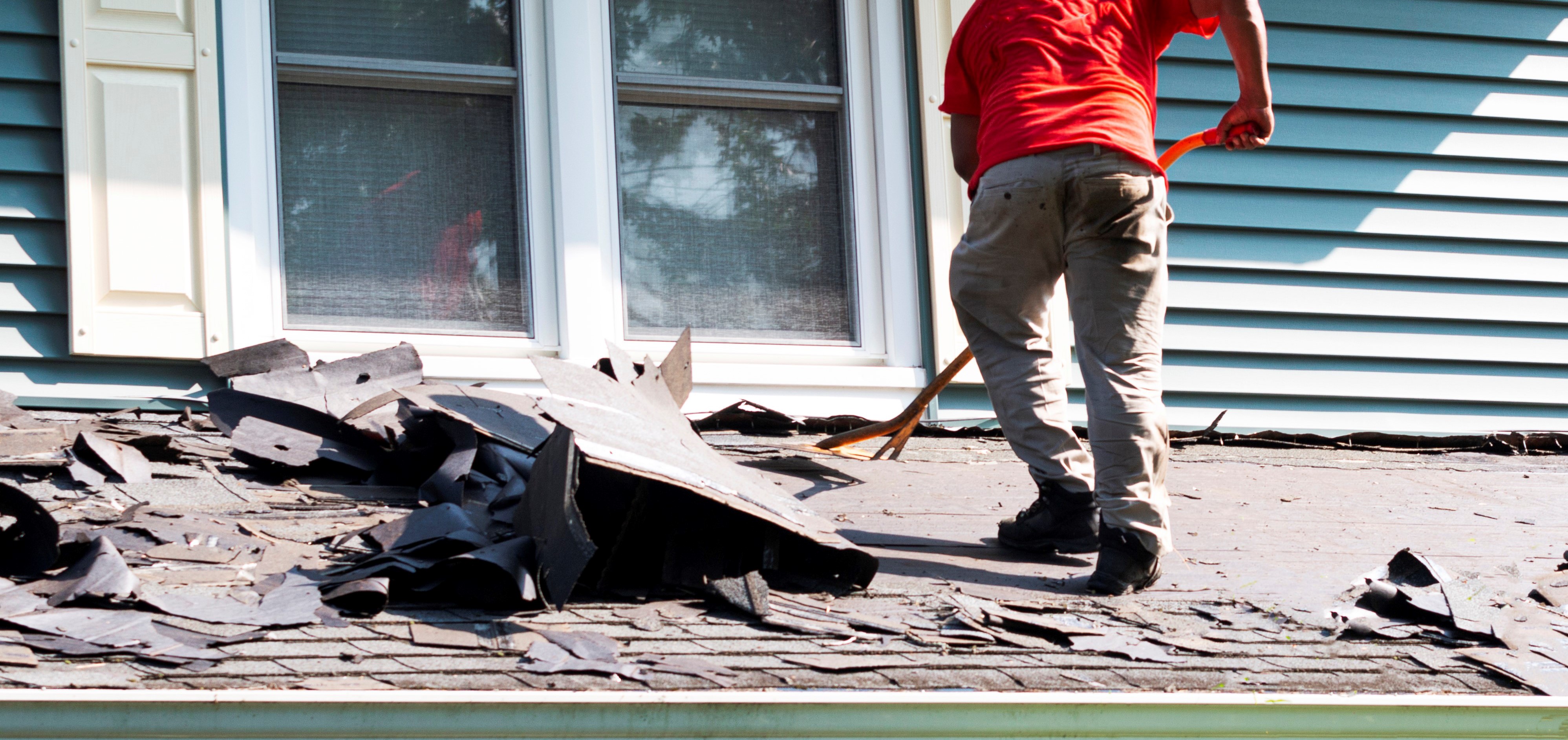 Worker removing old asphalt shingles from the roof