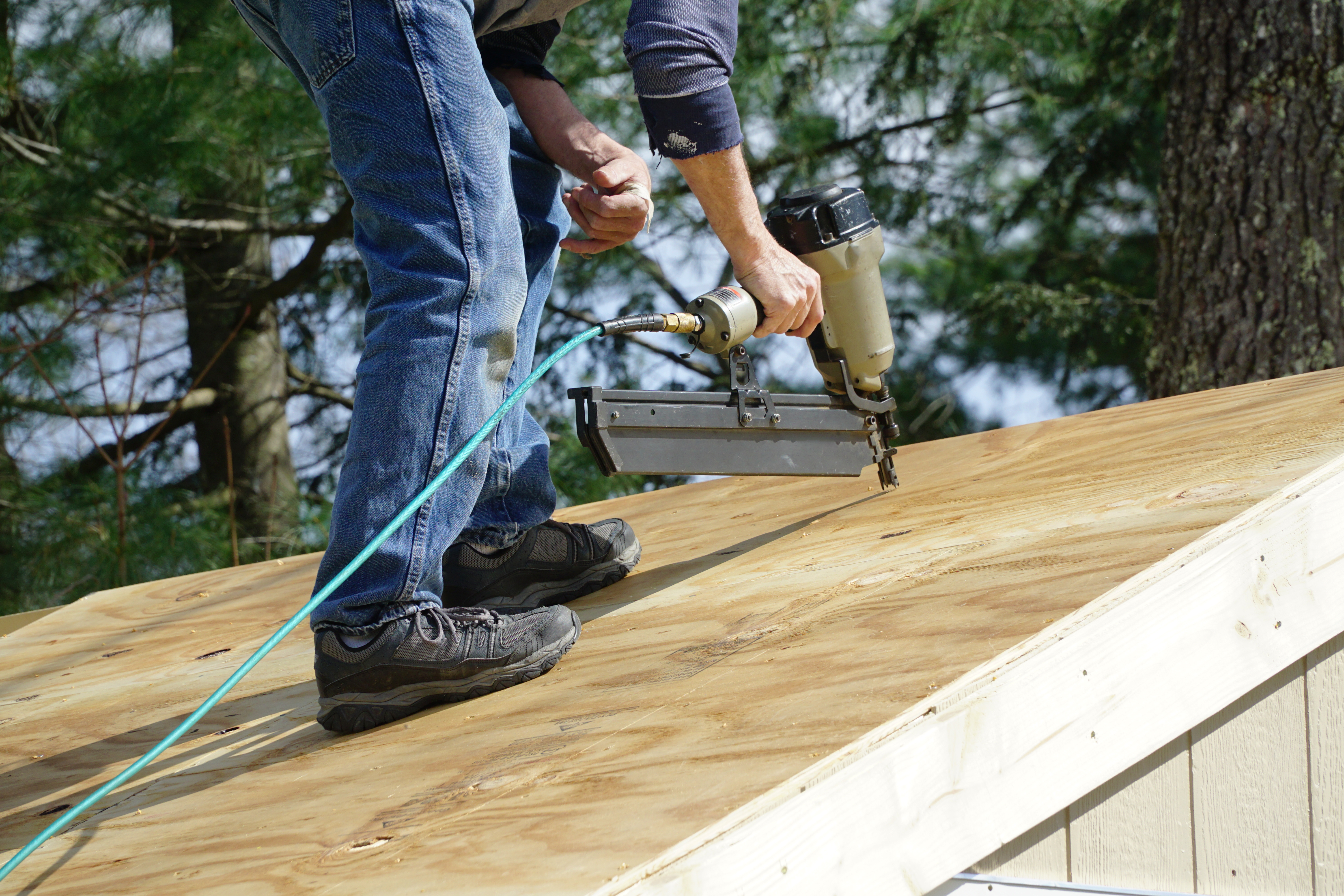 Contractor using a nail gun to attach wood panels to the roof