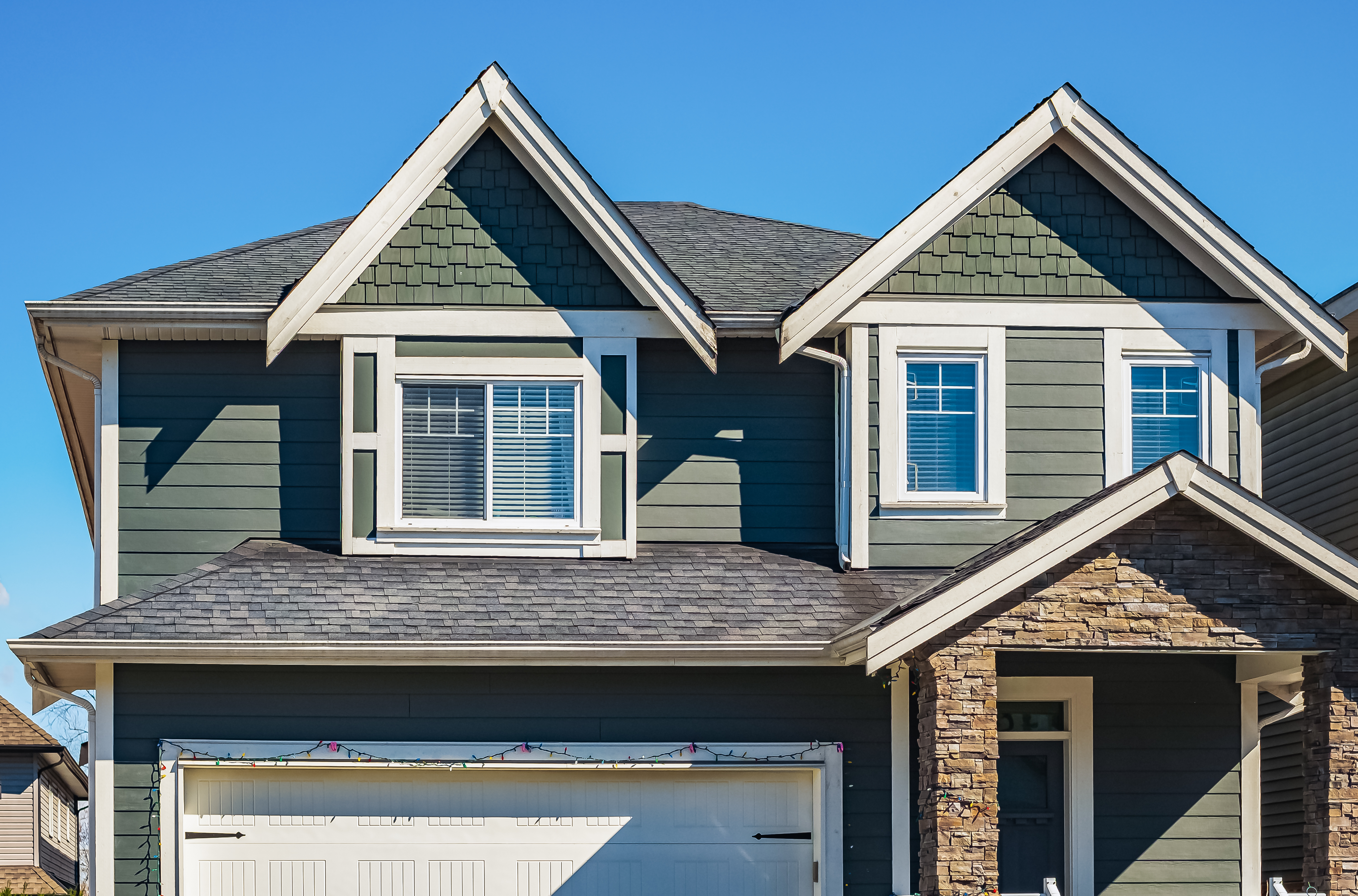 Dormer windows with white trim installed on a green-siding house