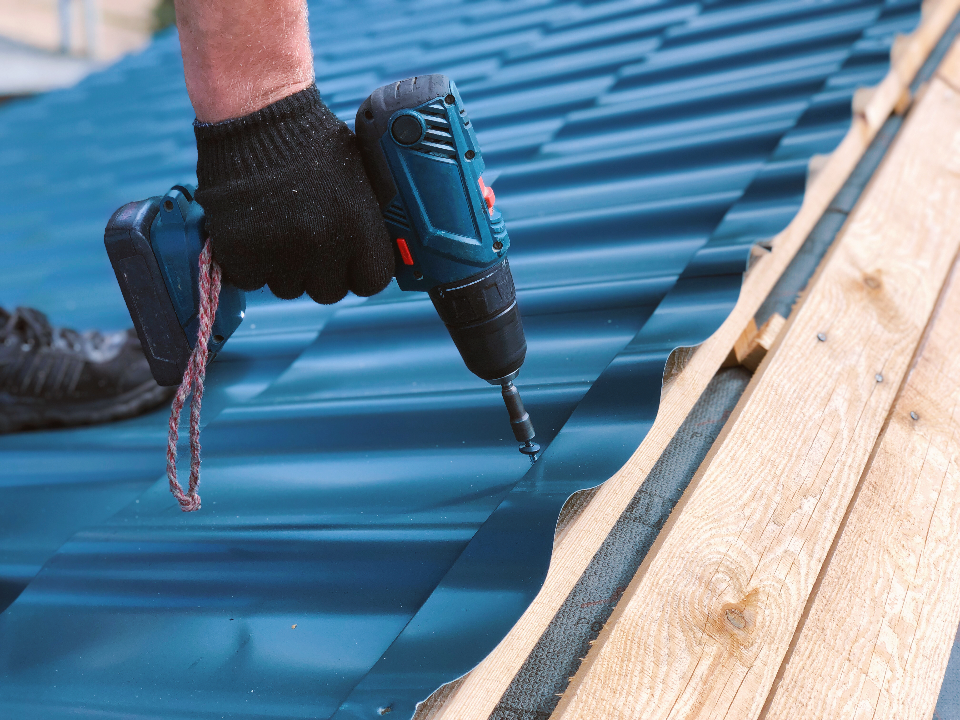Roofer using an electric screwdriver to attach a metal roof sheet