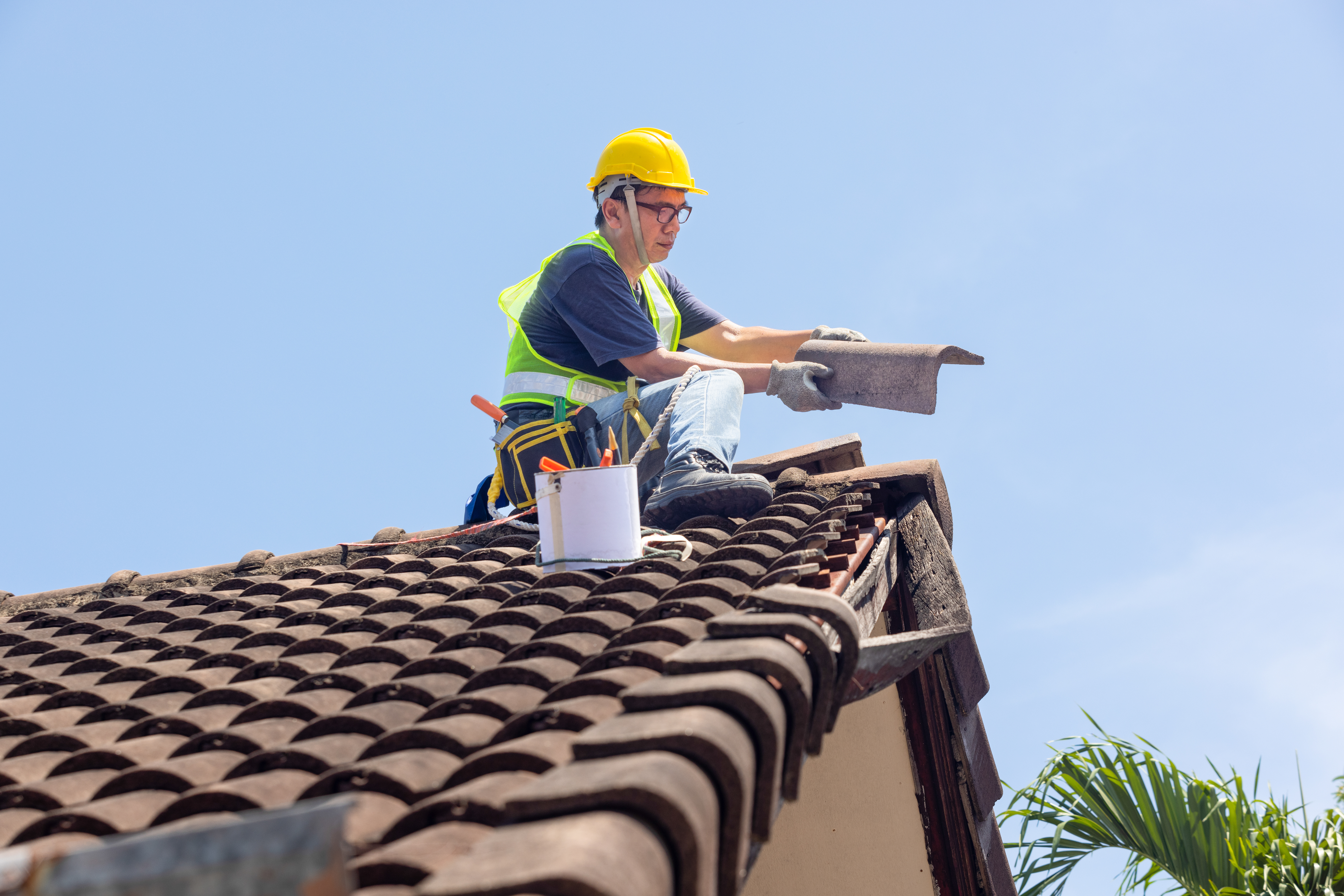 Roofer wearing safety gear repairing a tile roof