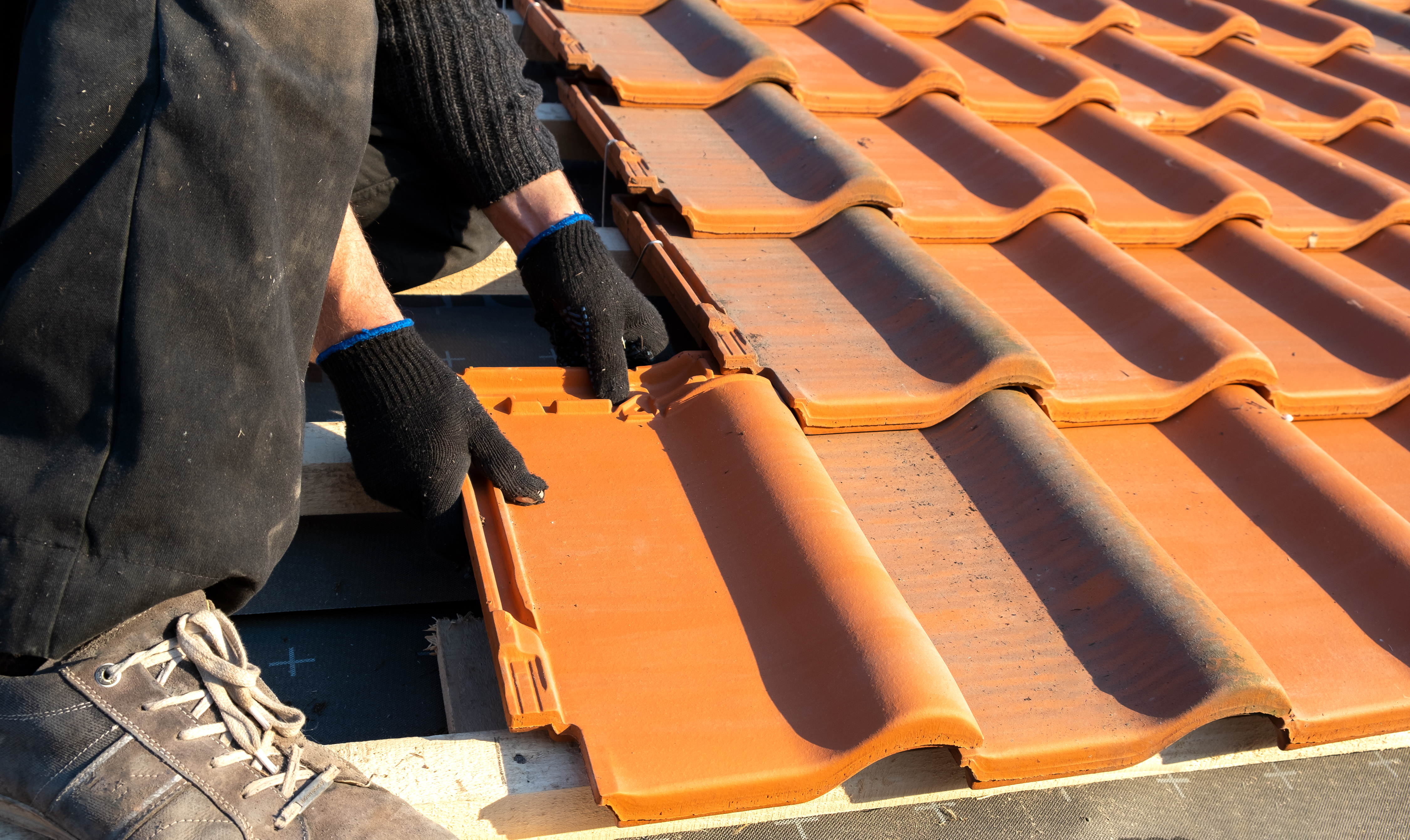 Worker installing new clay tiles on the roof