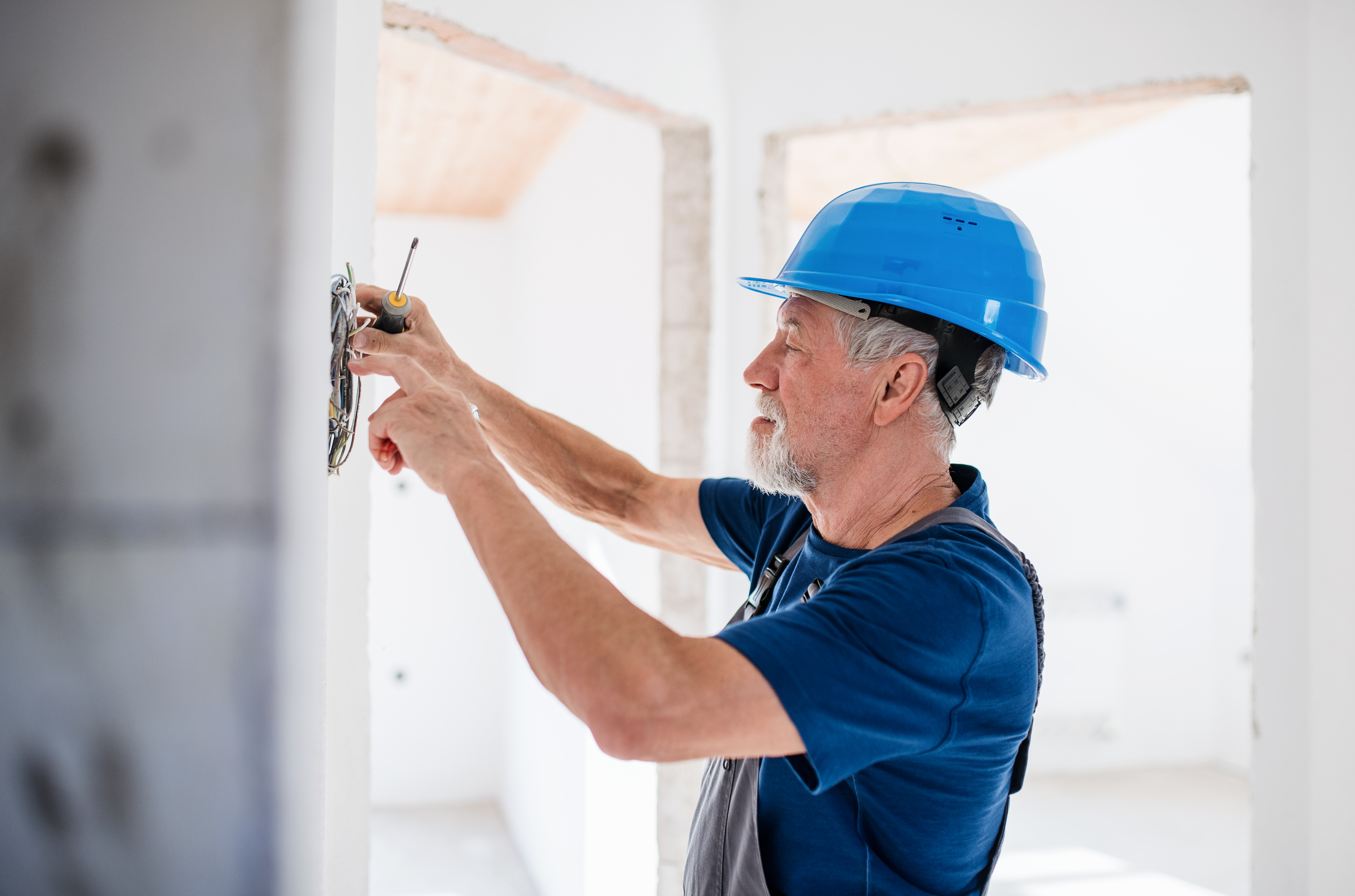 Senior man electrician with helmet working indoors on house construction site