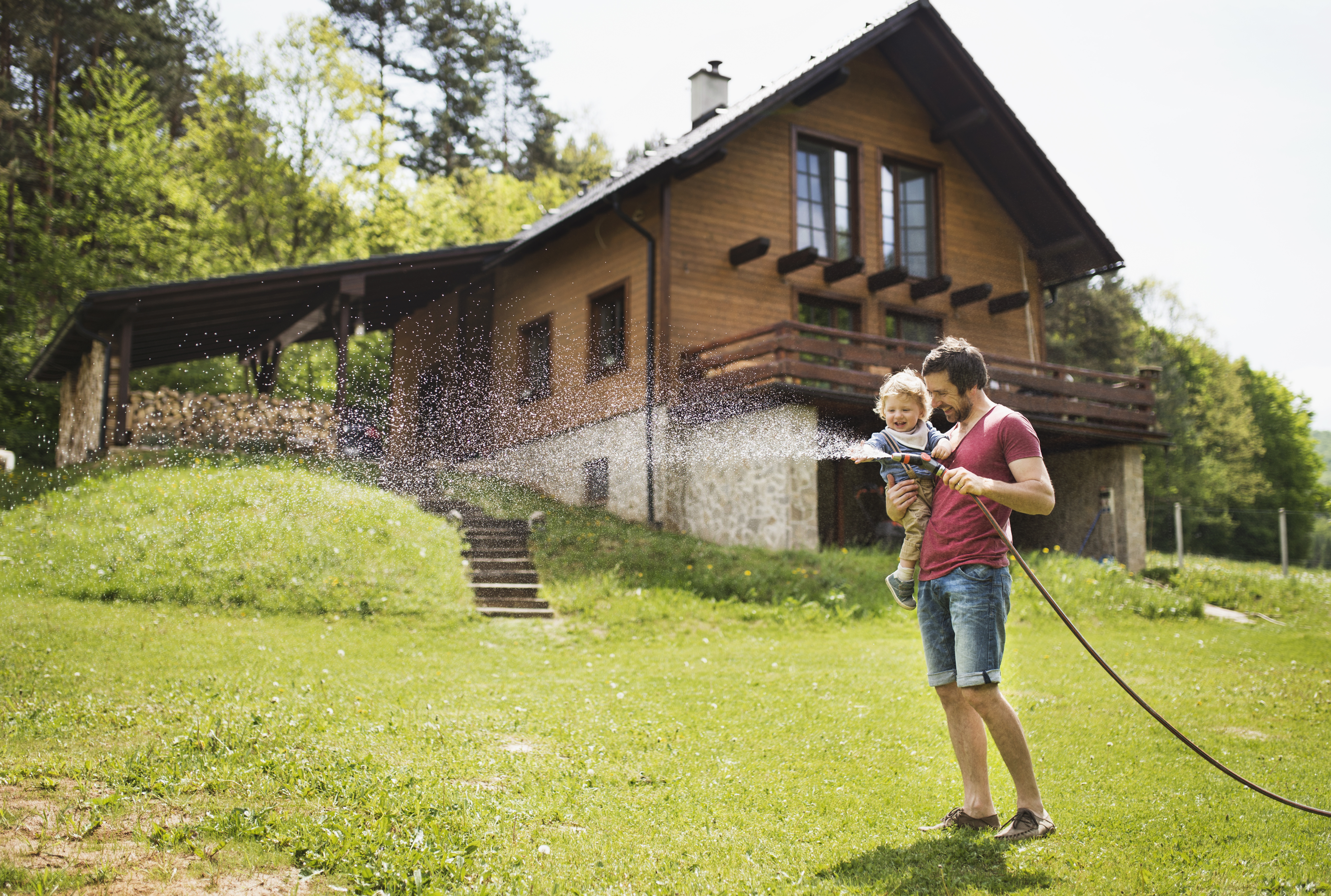 A man with his son watering the lawn in front of their home