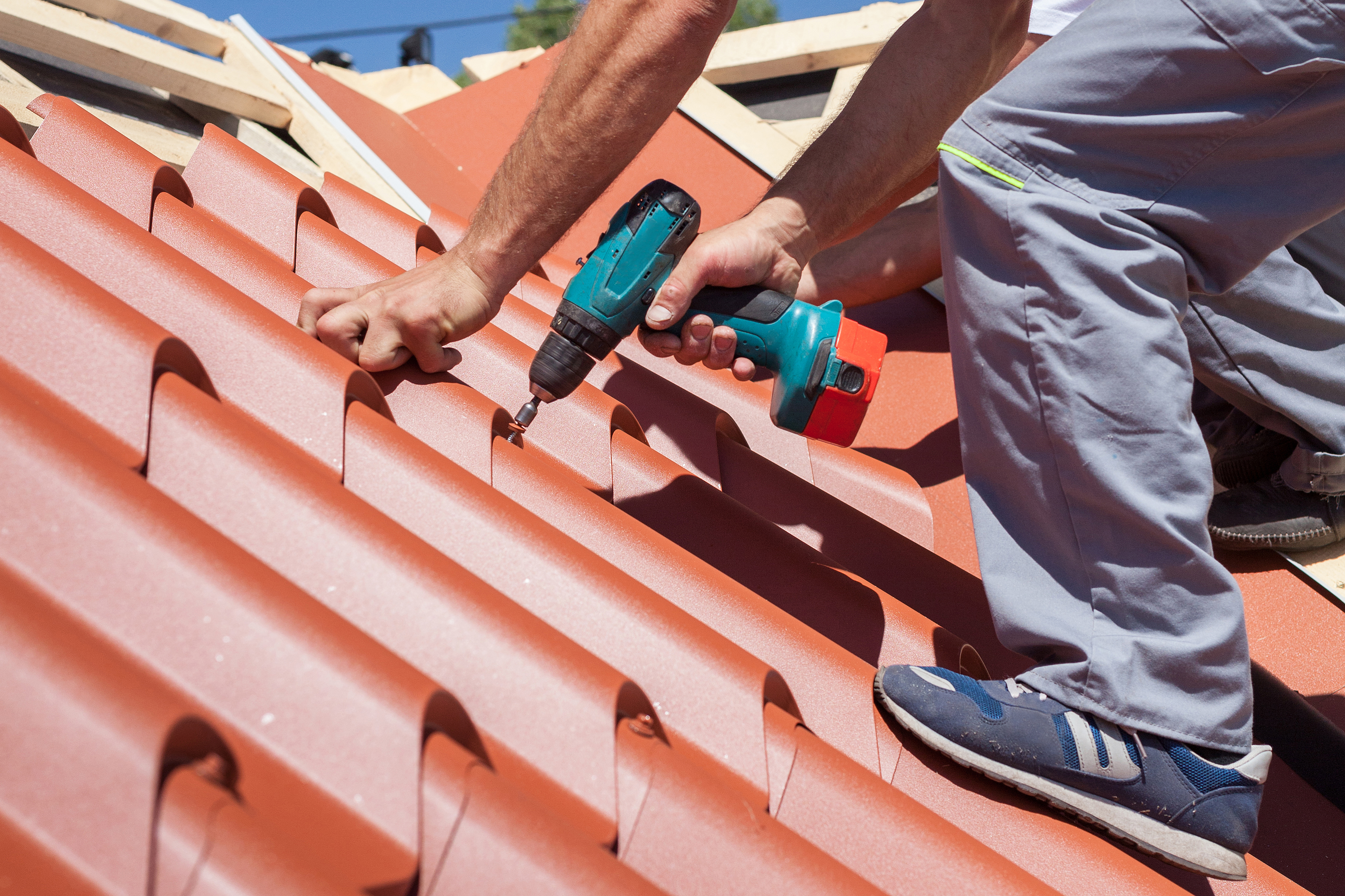Worker attaching red metal tiles to the roof of a house