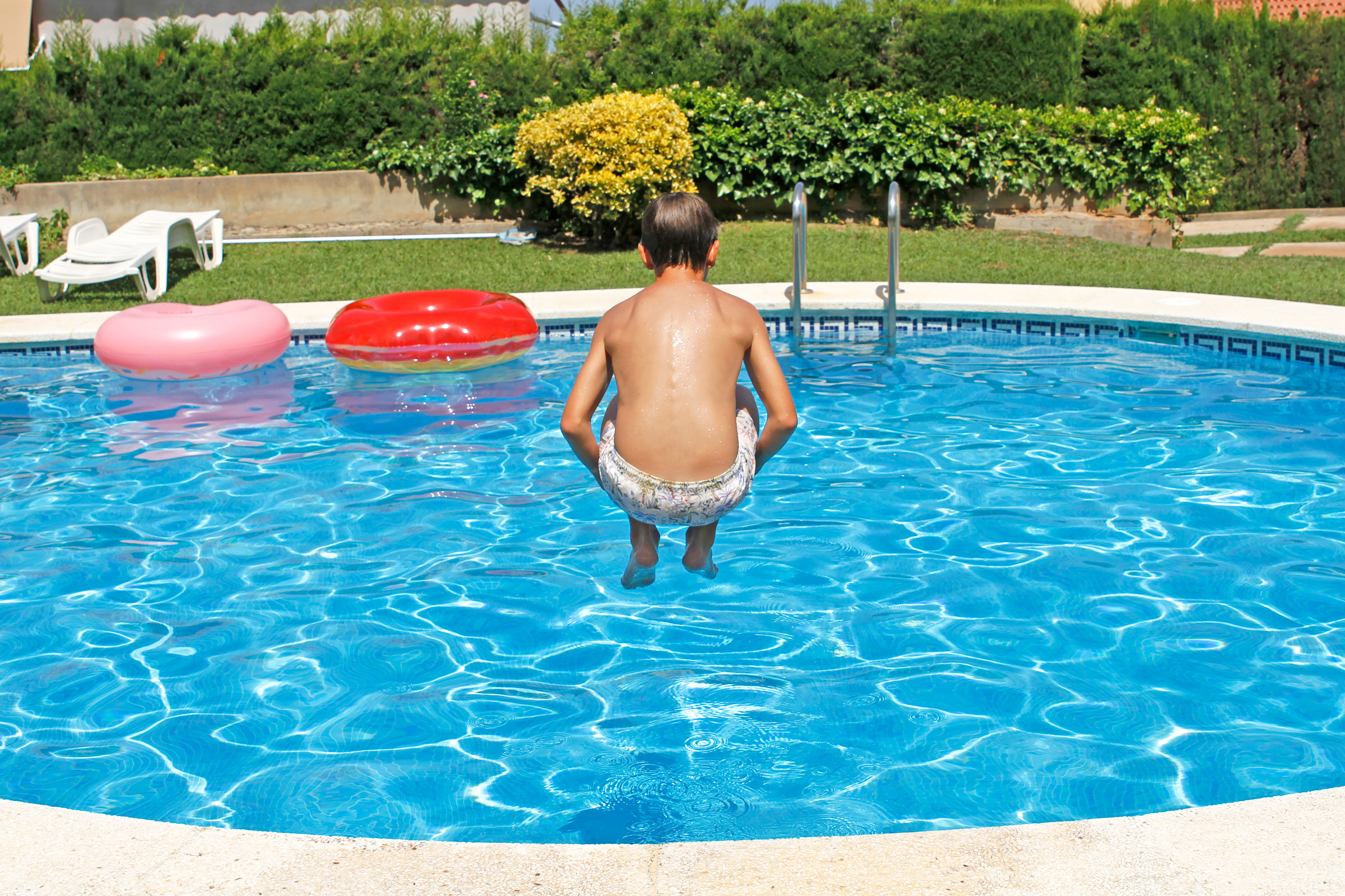 Boy jumping into an inground swimming pool