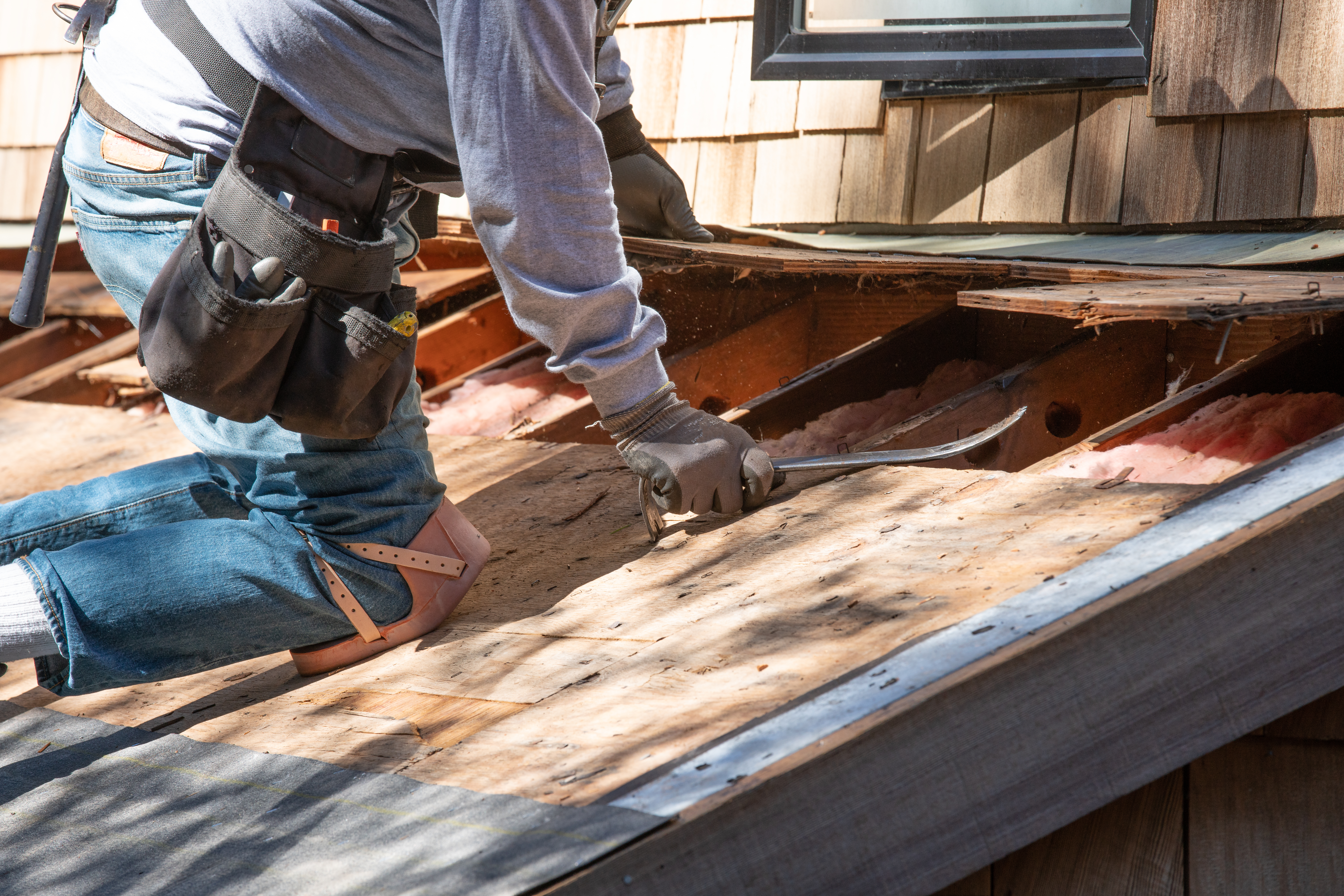 Worker using a prybar to remove damaged roof sheathing