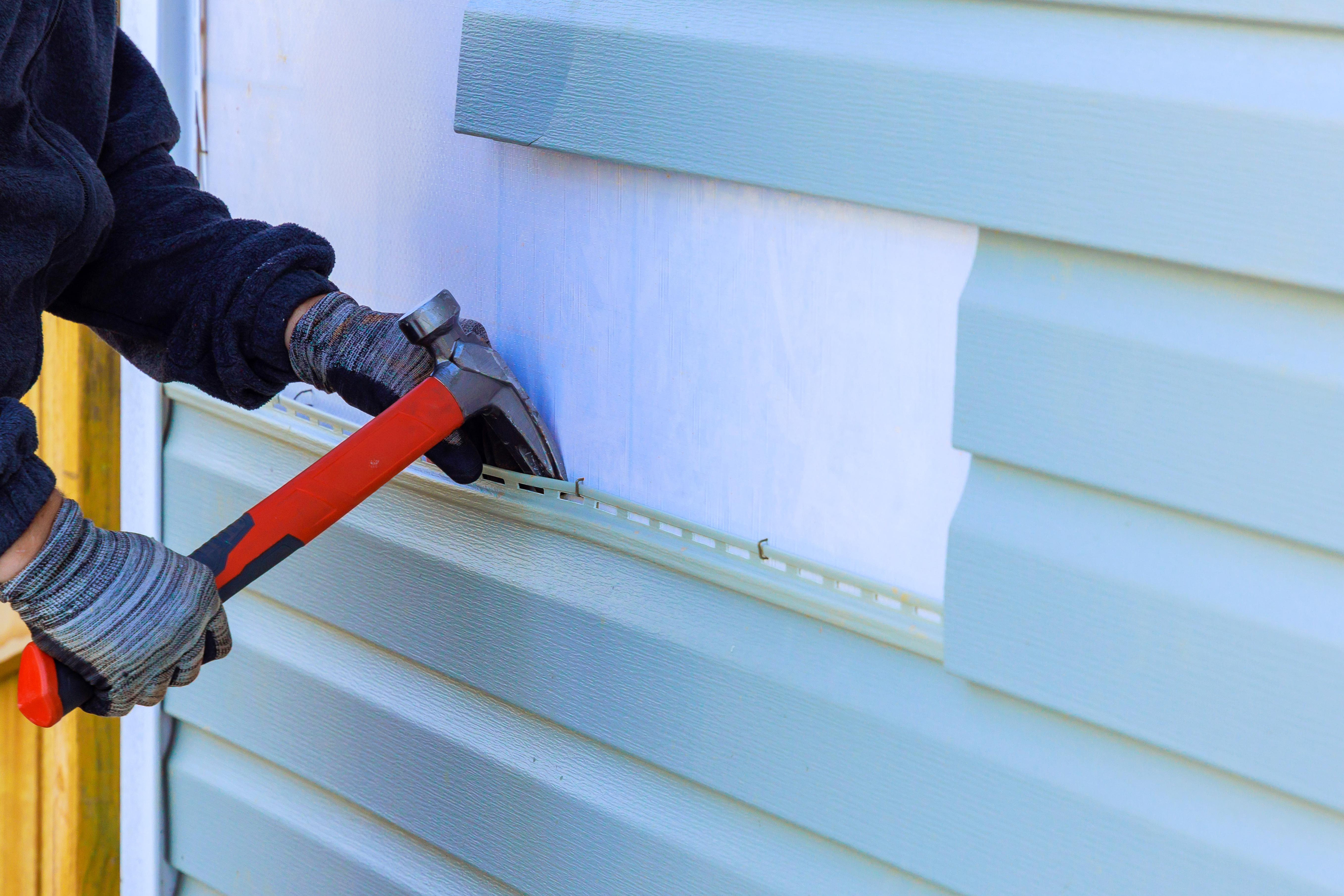 Worker using a hammer to install vinyl siding