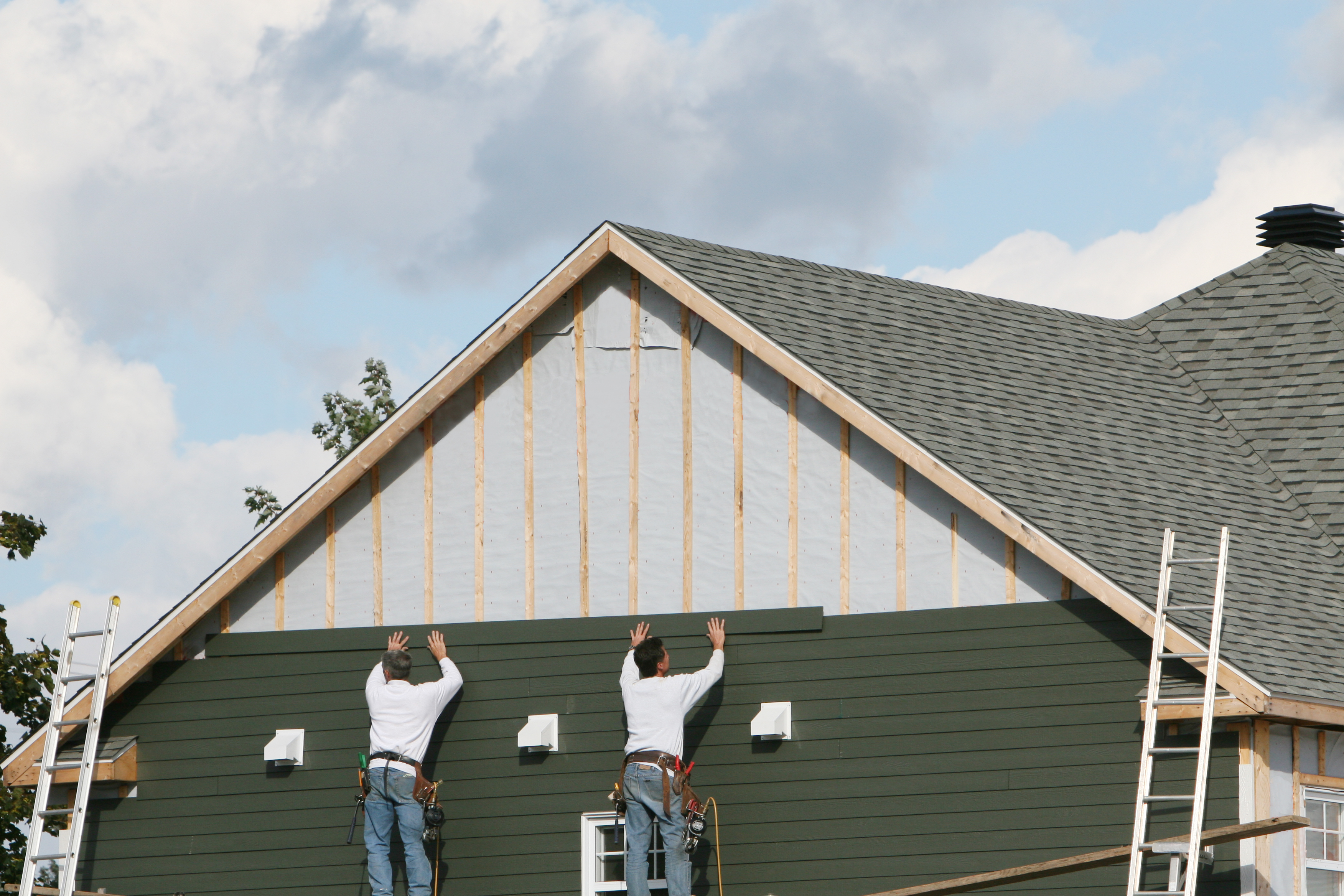 Two men installing green paneling to a house 
