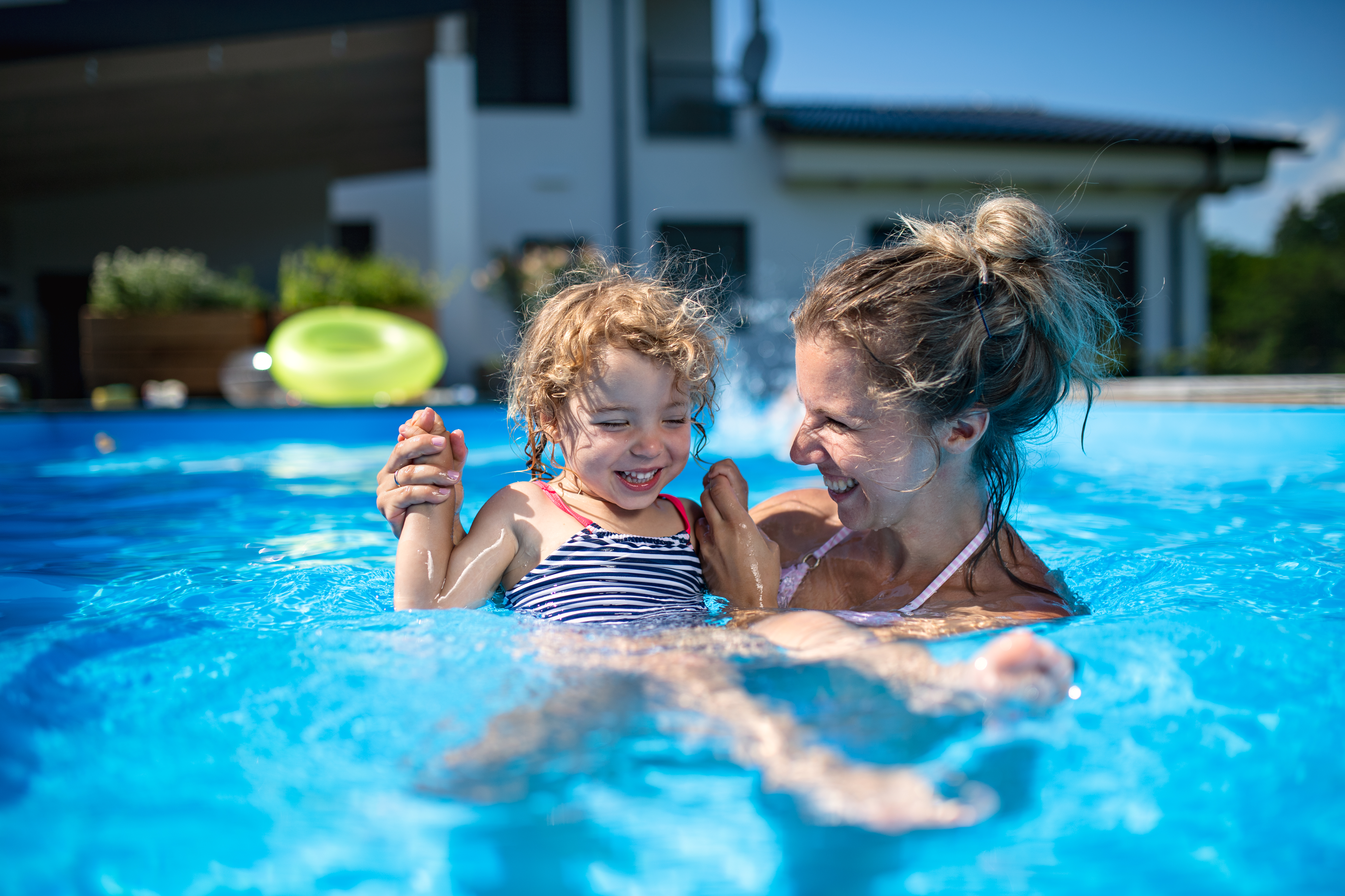 mother with small daughter playing in swimming pool 
