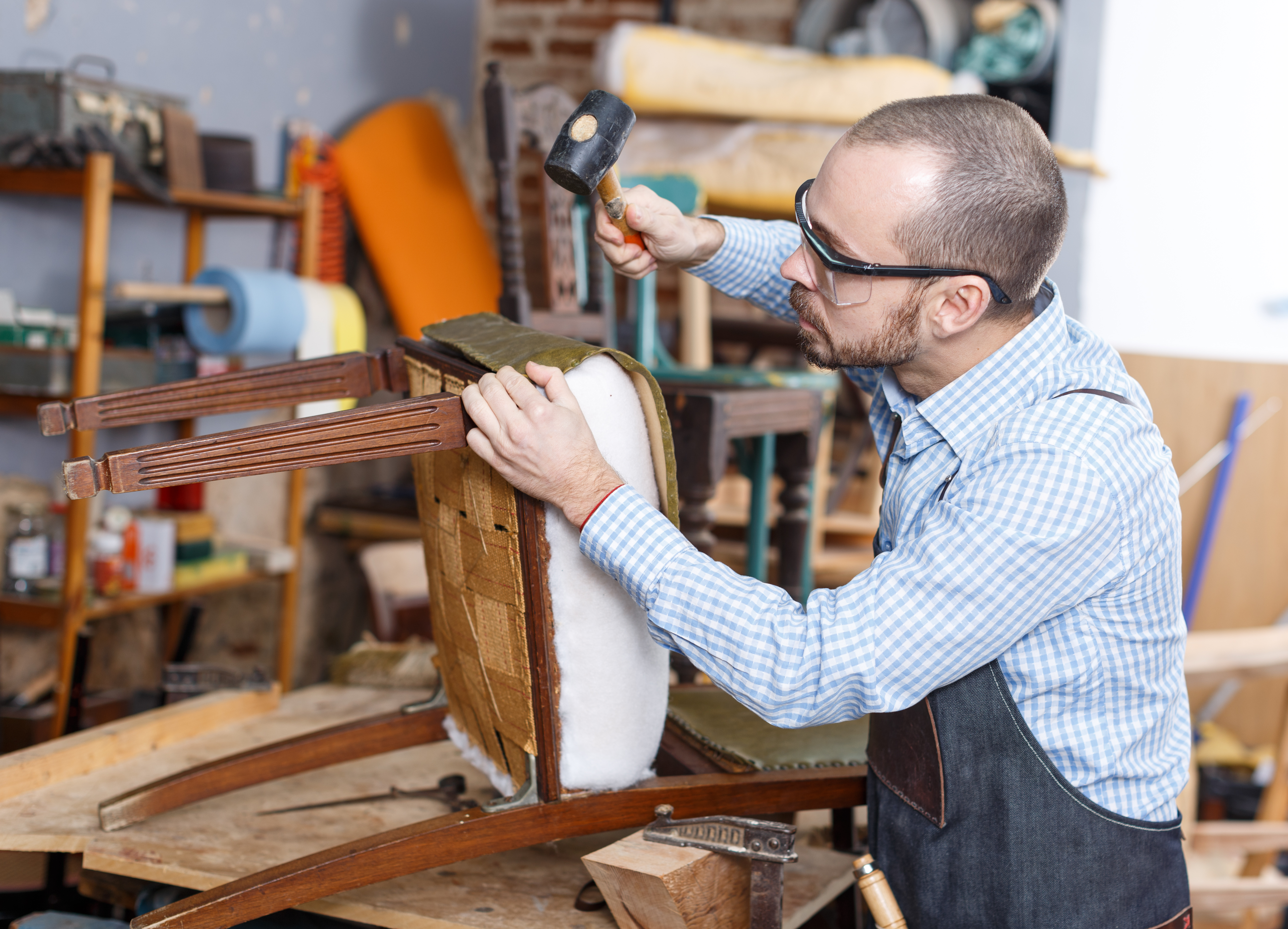 Craftsman carefully working to furniture upholster a chair, restoring its fabric and cushioning for a fresh, new look