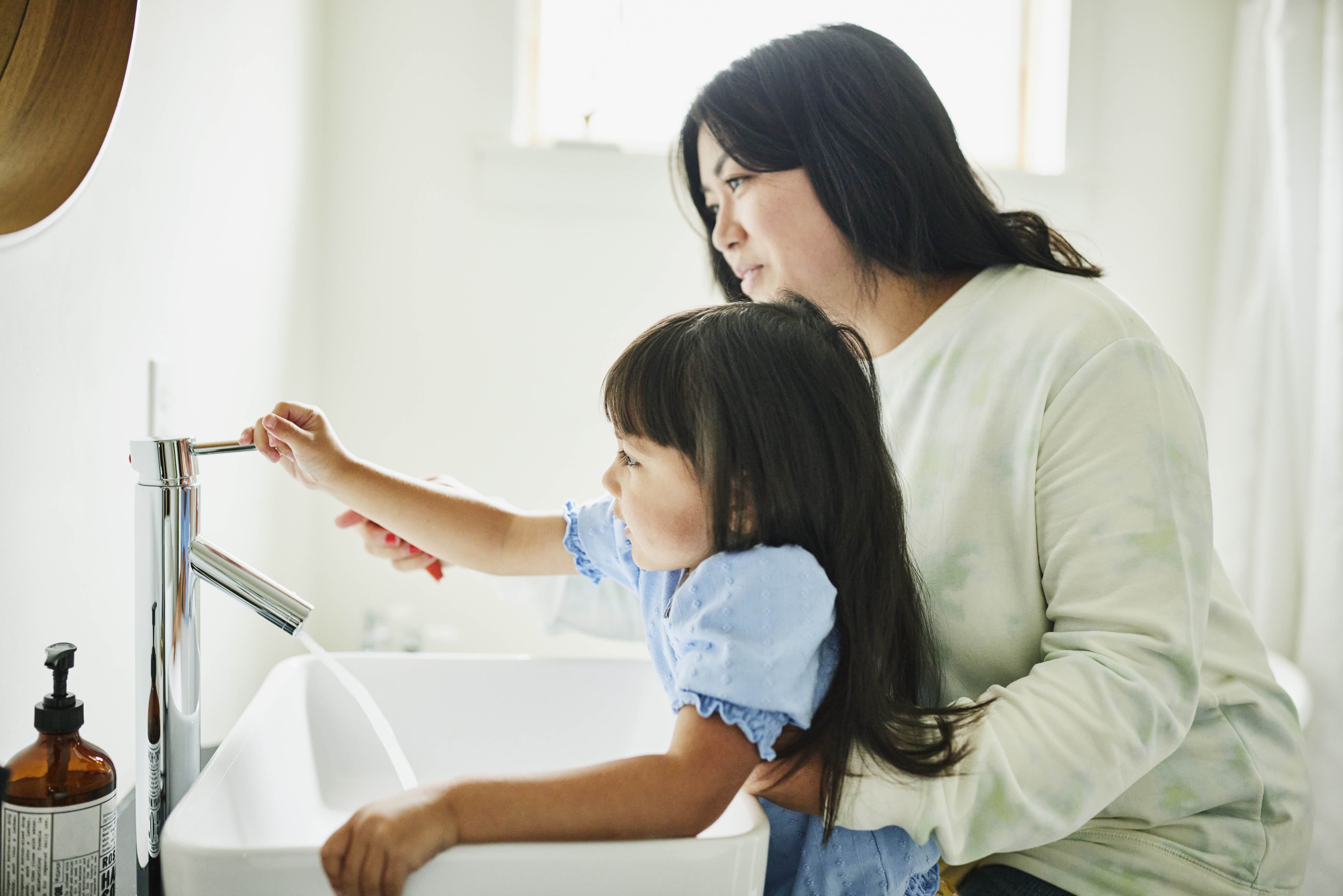 Mother helping little daughter wash her hands