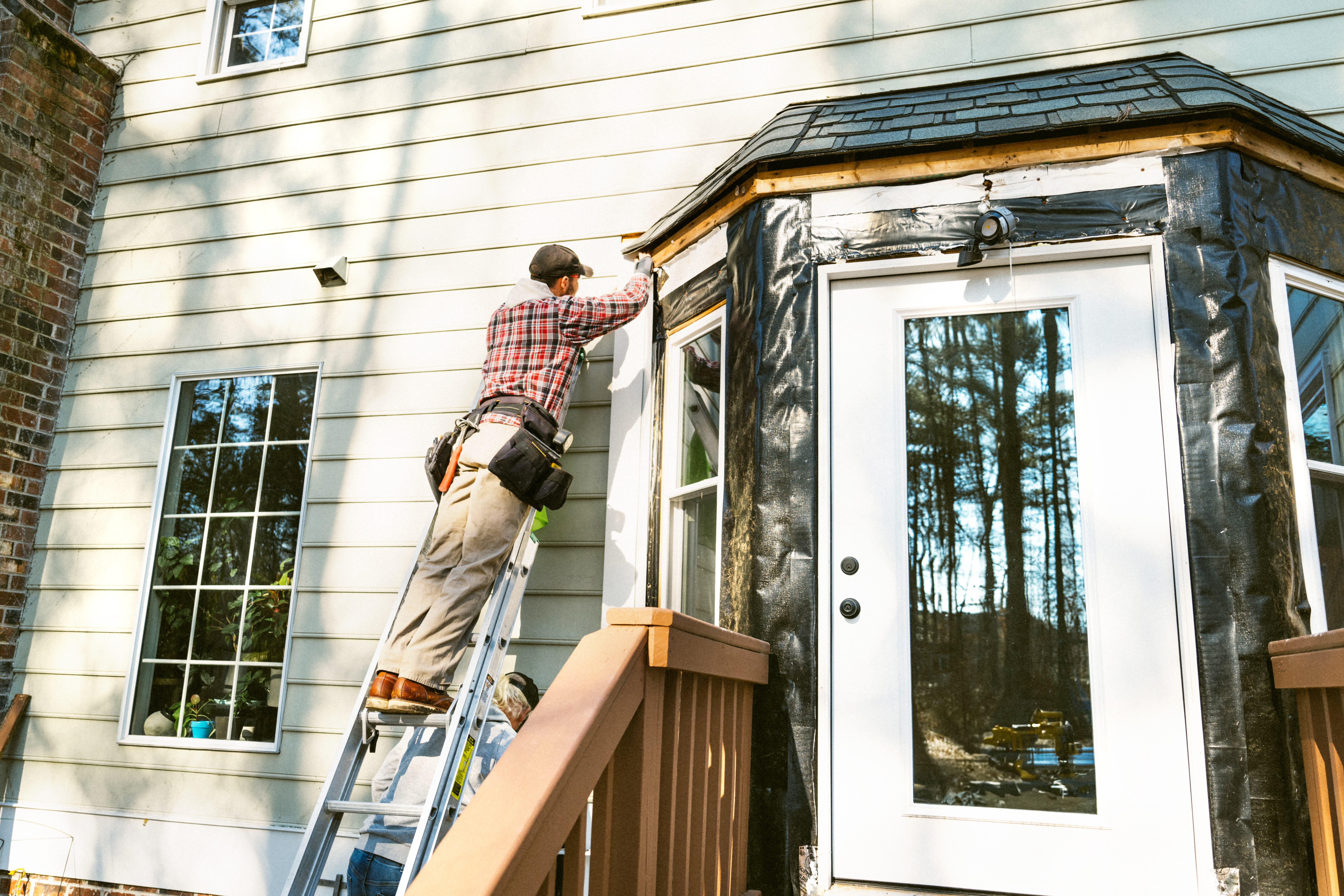 Worker on a ladder repairing wood siding 