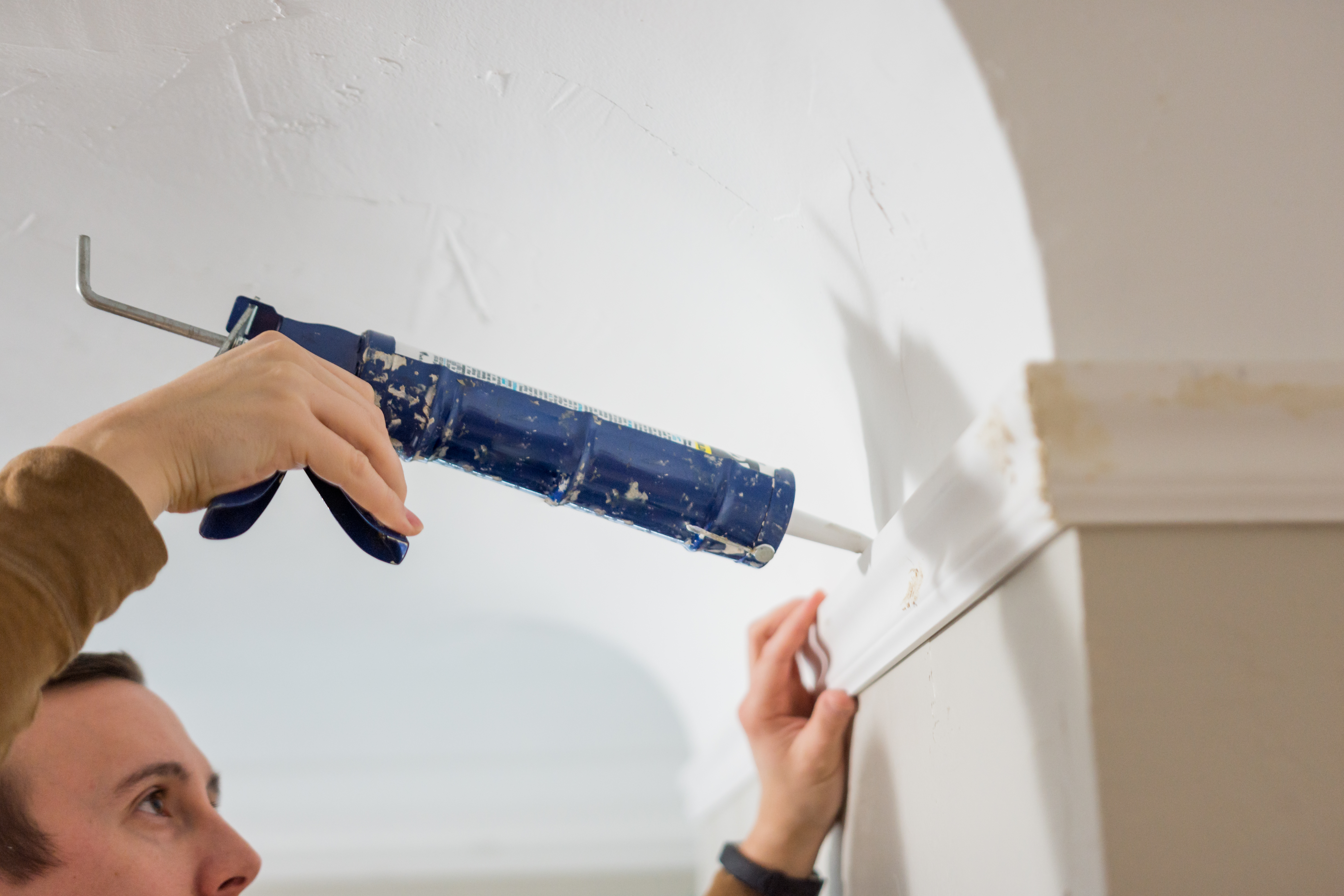 A person caulking a crown molding 