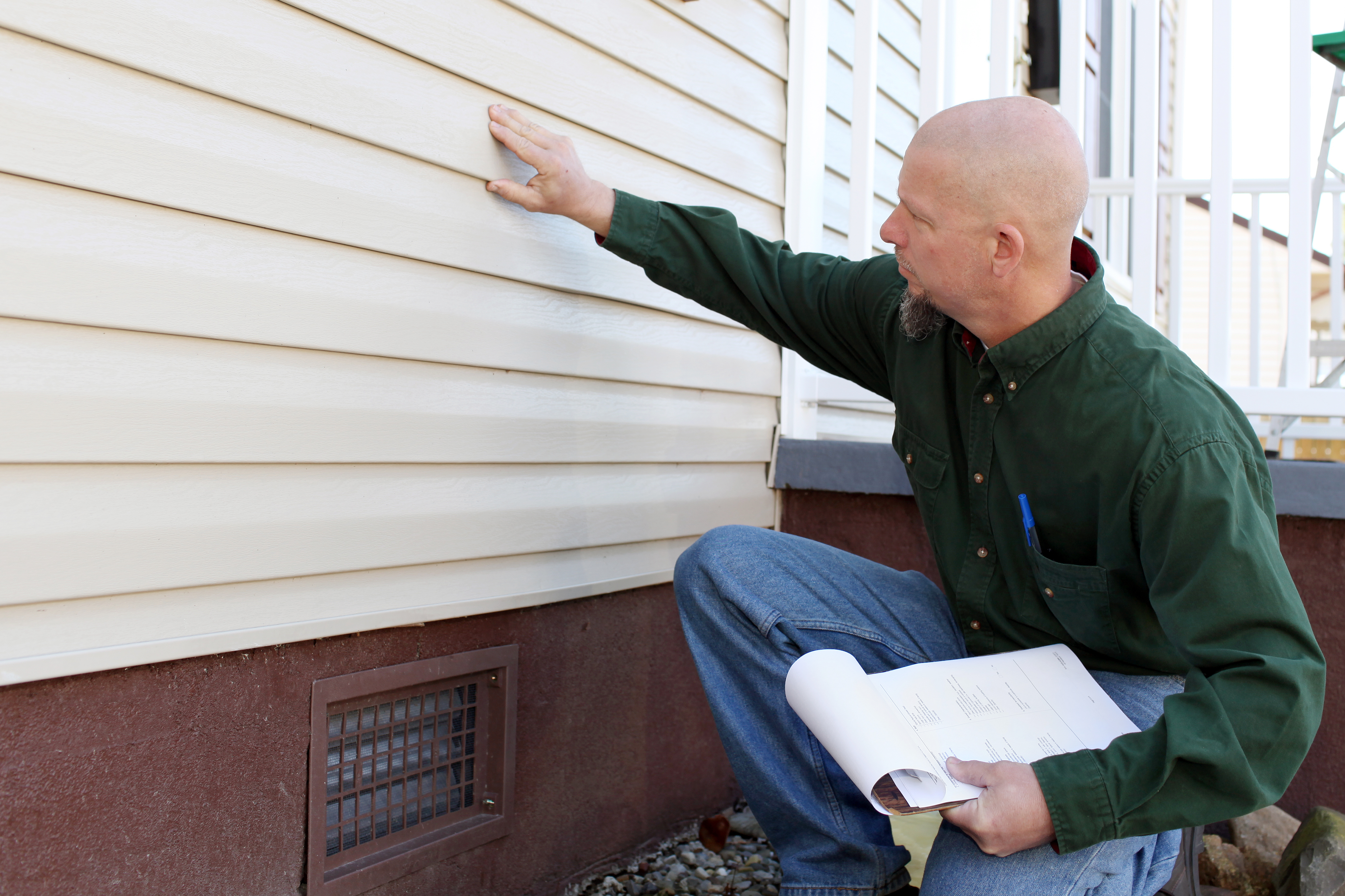 Contractor holding a clipboard and inspecting the house siding