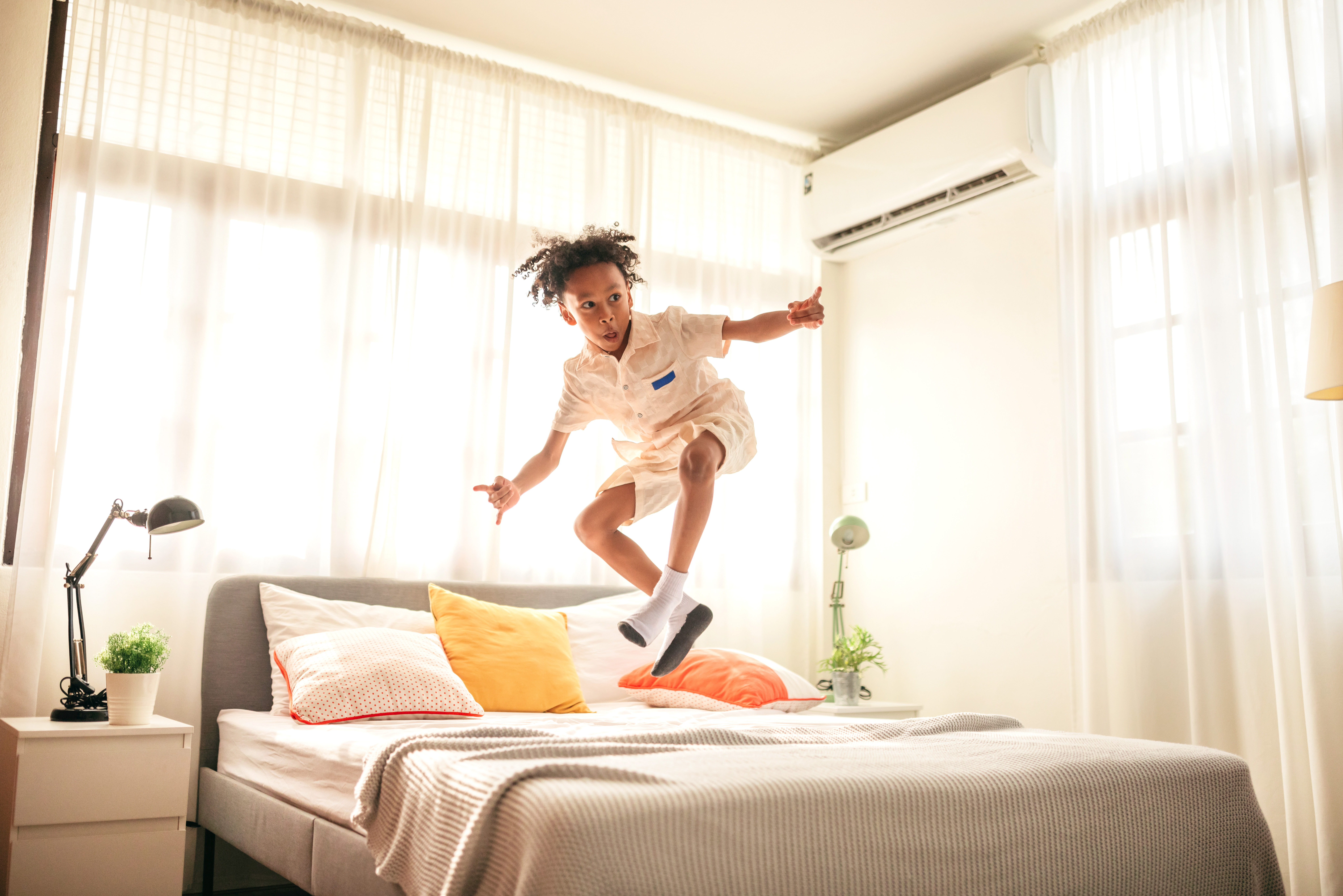 Boy jumping on the bed in a bedroom with AC