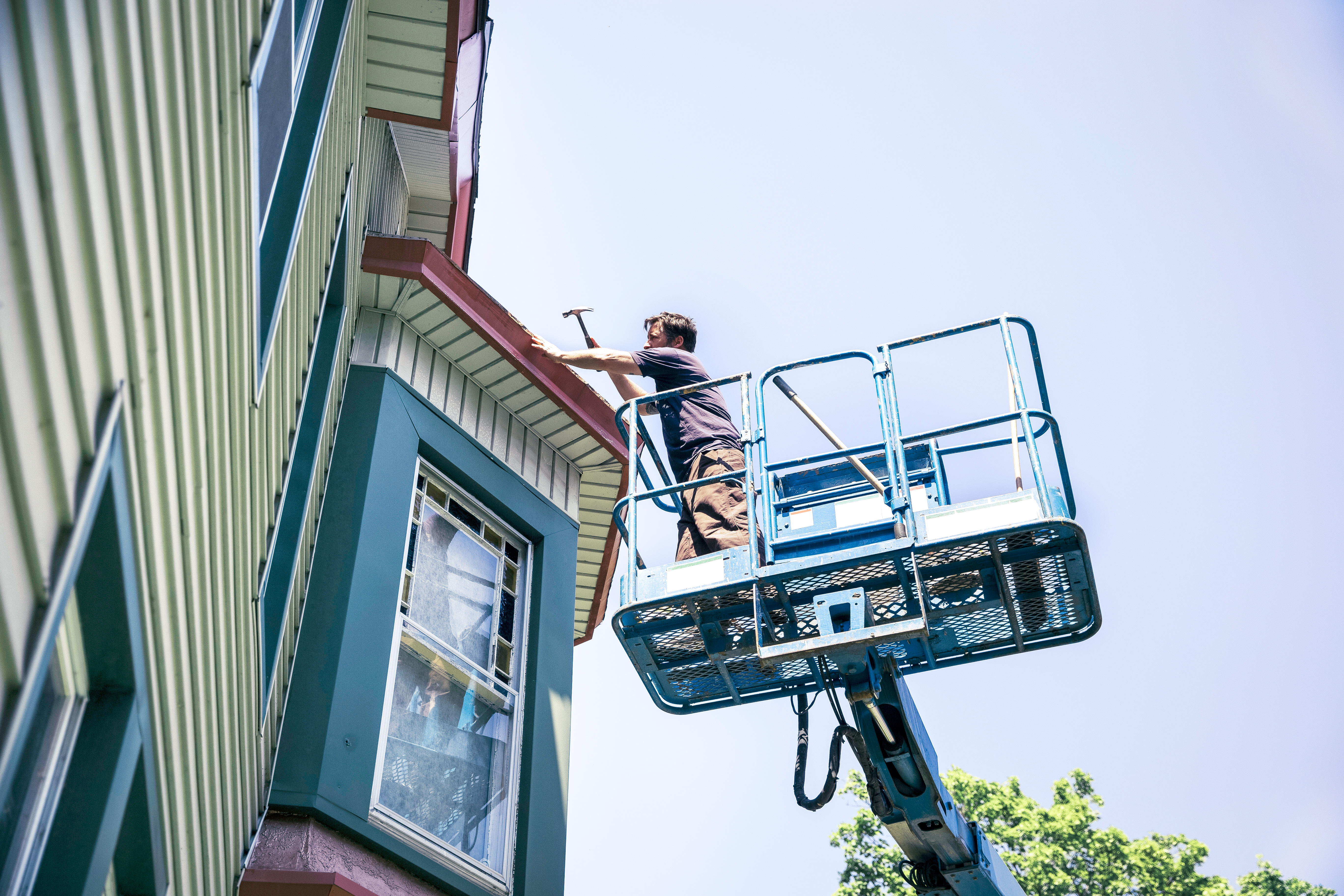 Roofer in a basket lift repairing the roof of a Victorian house