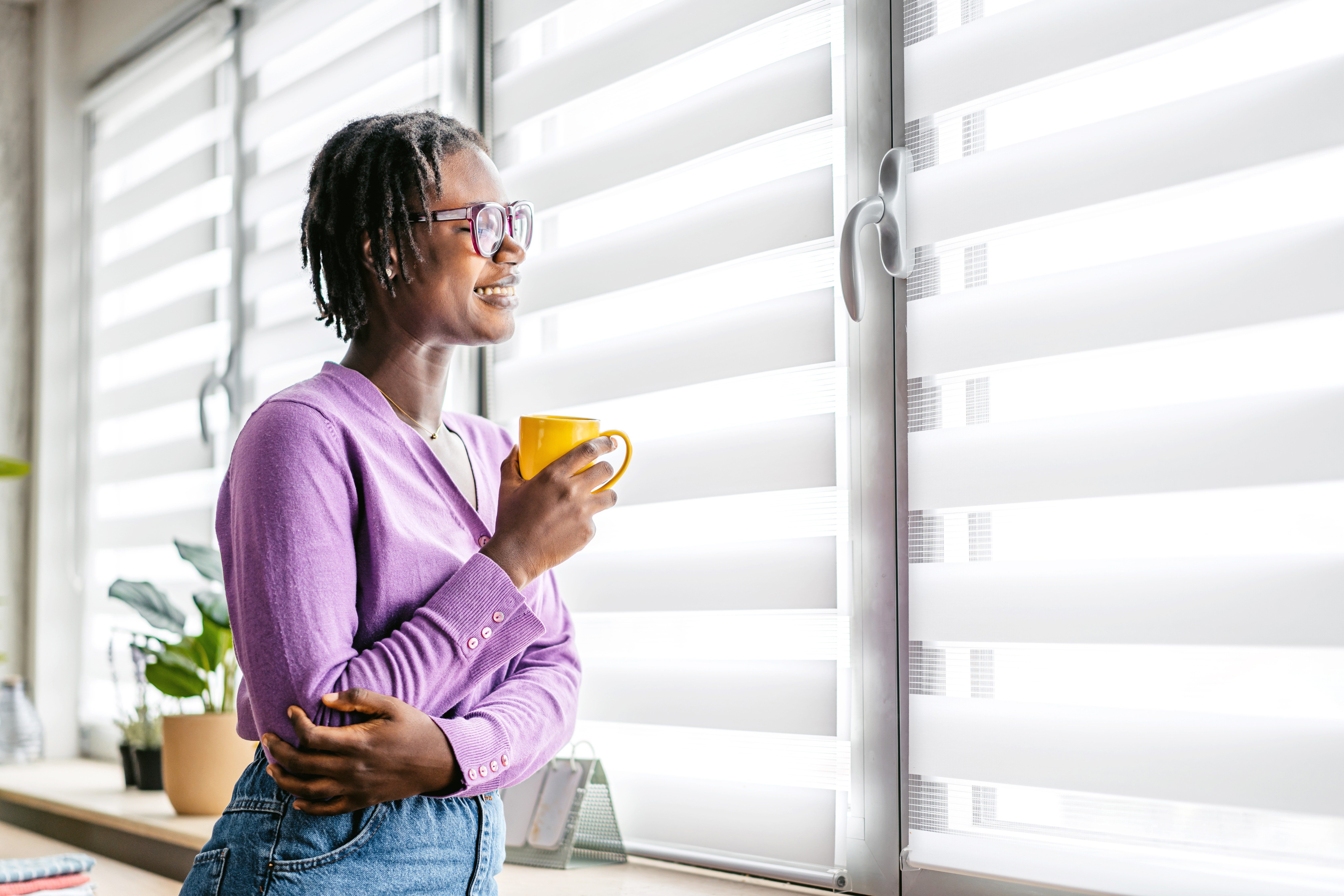 Woman drinking coffee and looking out a window with blinds  