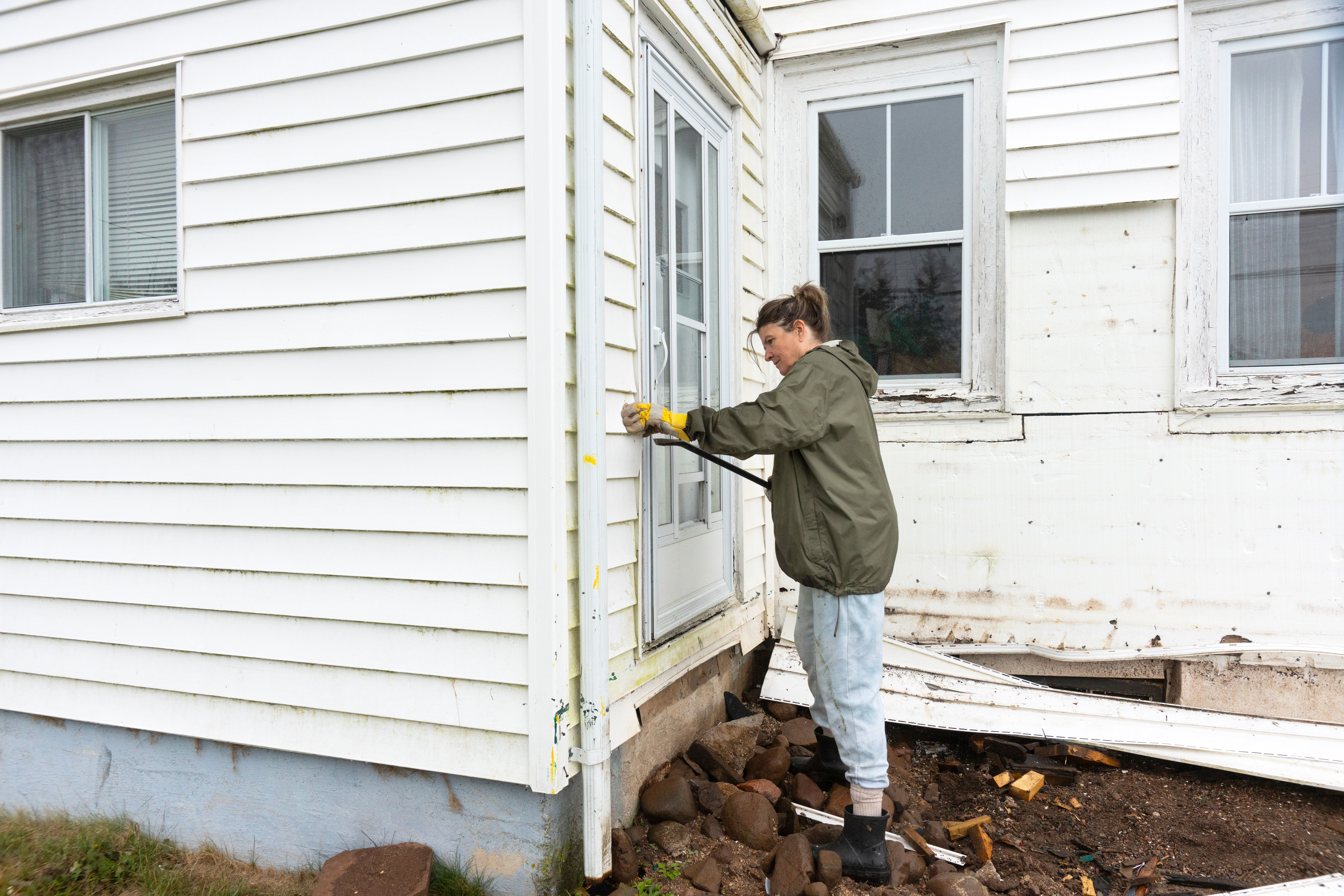 Woman removing old vinyl siding from a house  