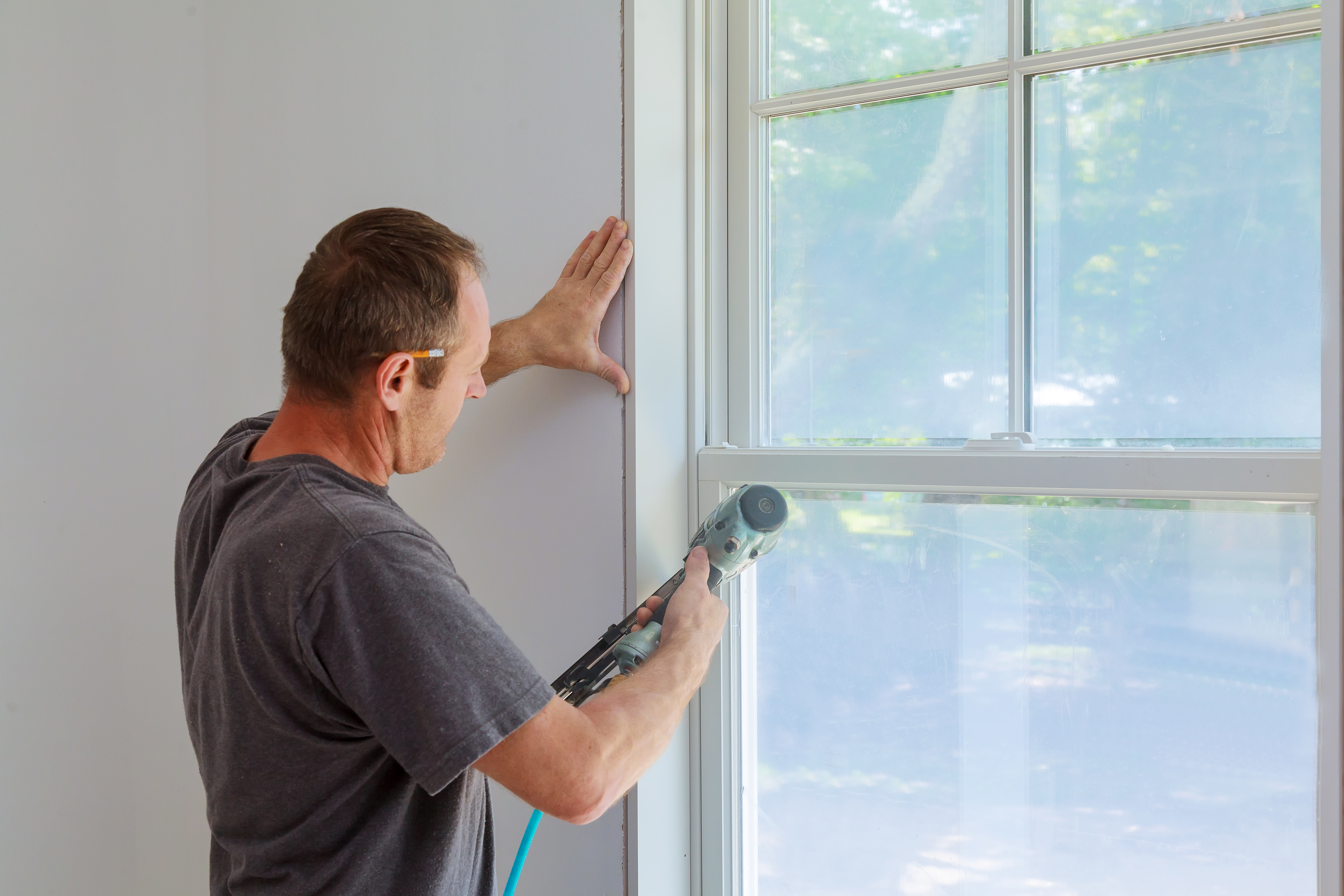 Worker using a nail gun to install a wood window trim