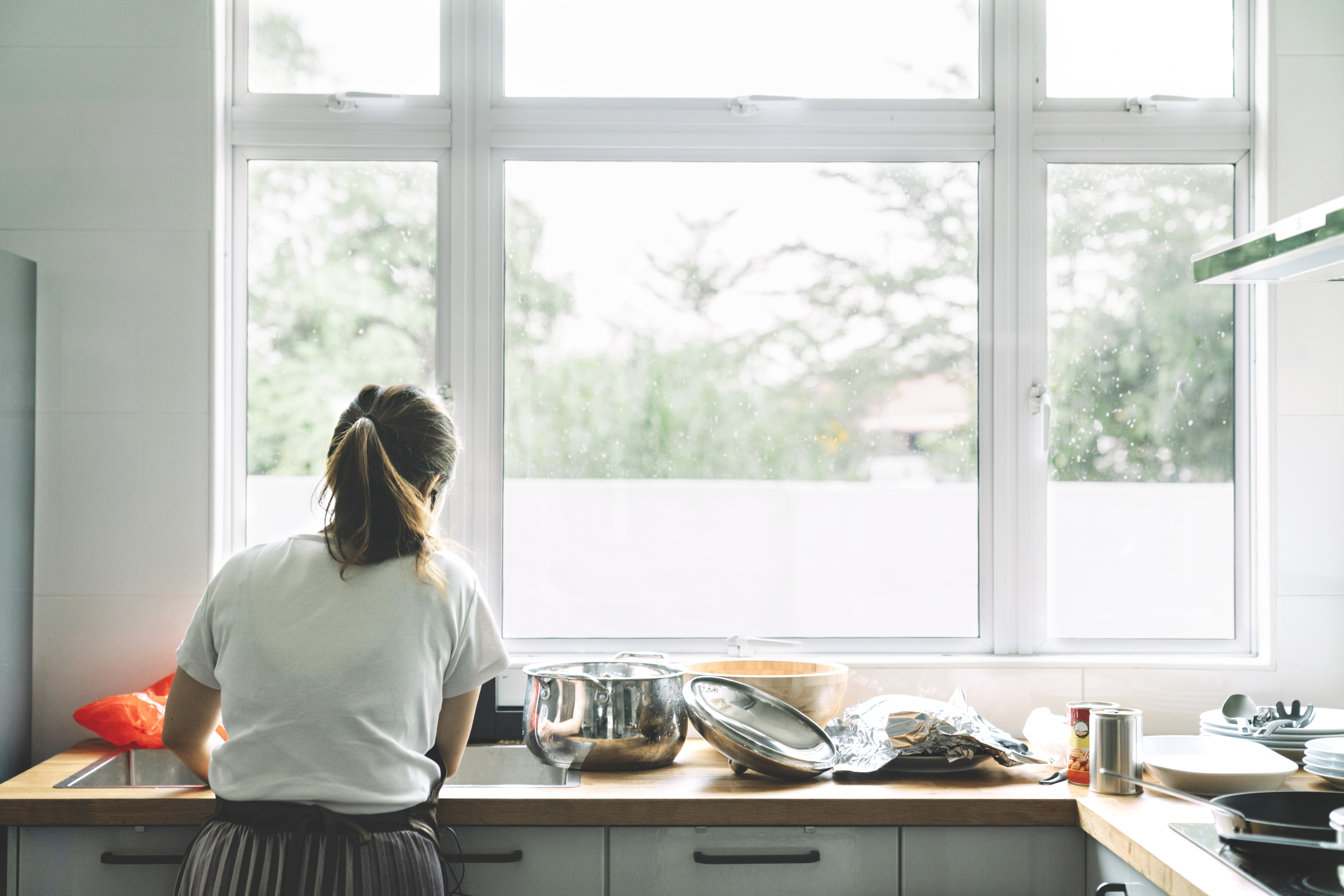  Woman standing in front of a large casement window is washing dishes 